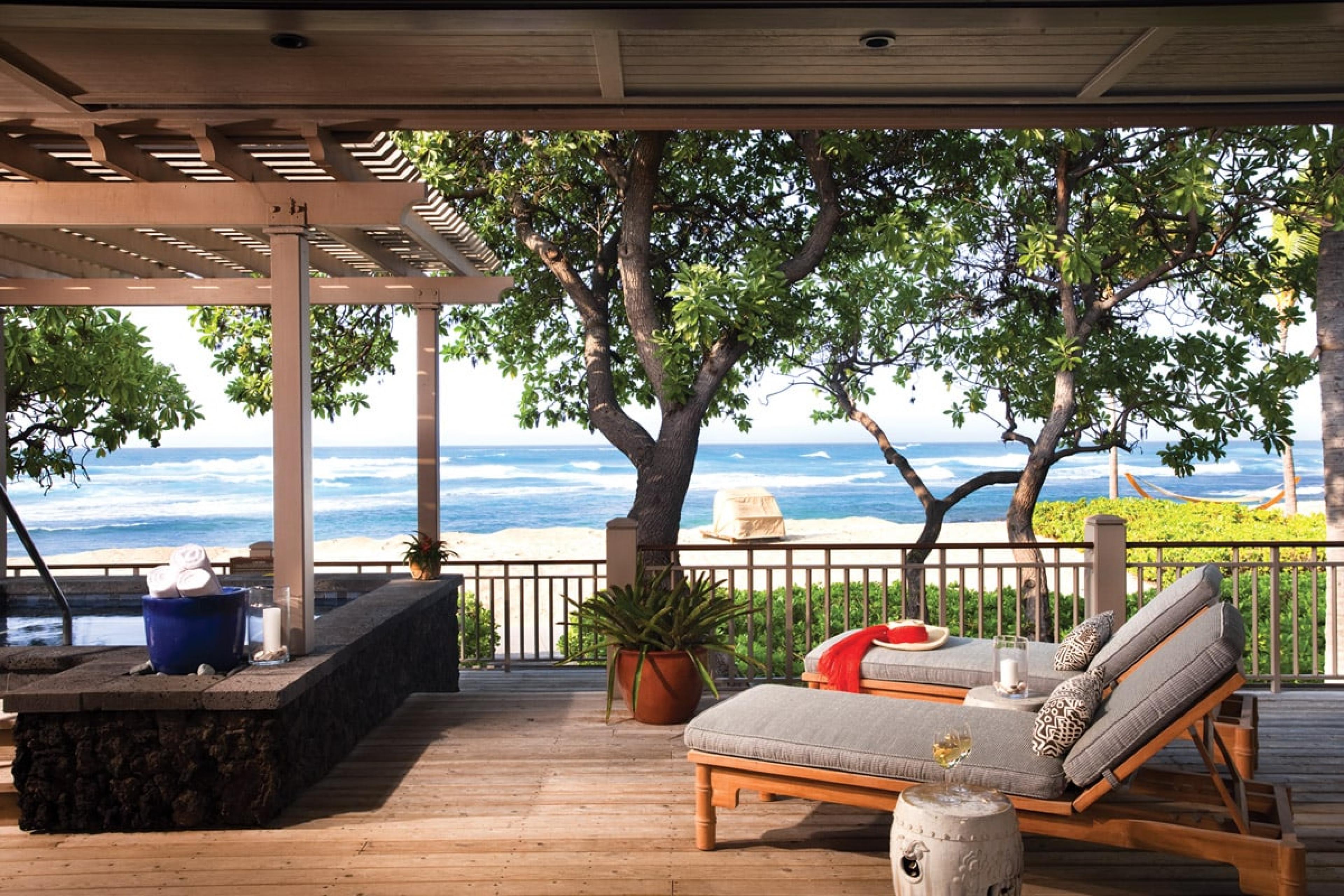covered terrace in hawaii with two reclining lounge chairs overlooking beach through trees