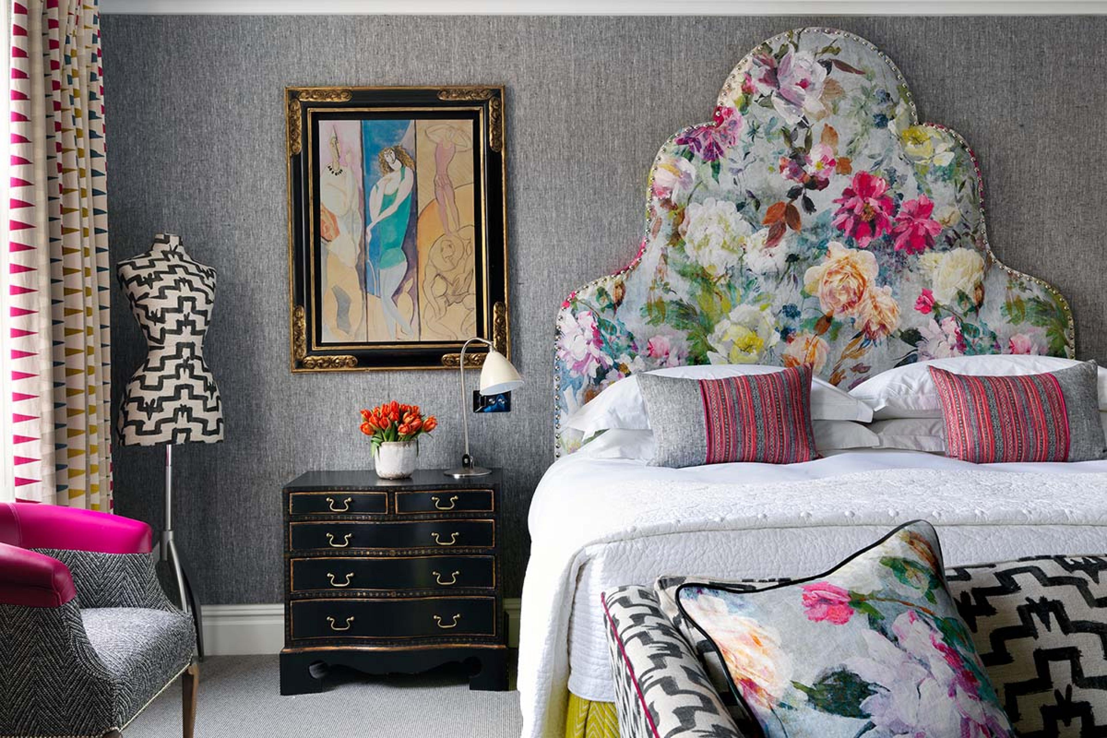 bedroom with a colorful floral headboard and a painting on the gray wallpaper