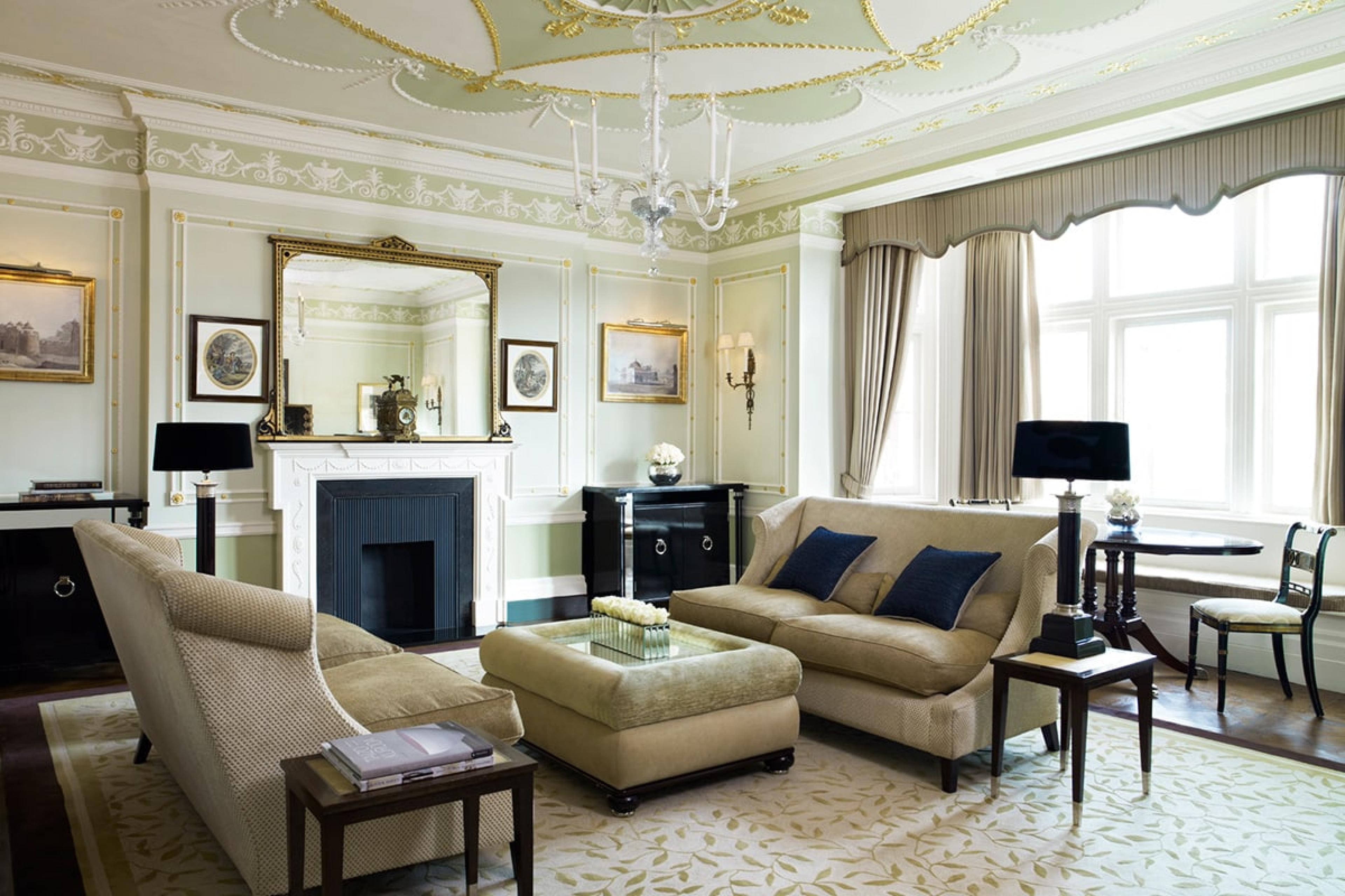 luxurious living room of a suite in a grand traditional london hotel with light-green accents and a white and black fireplace