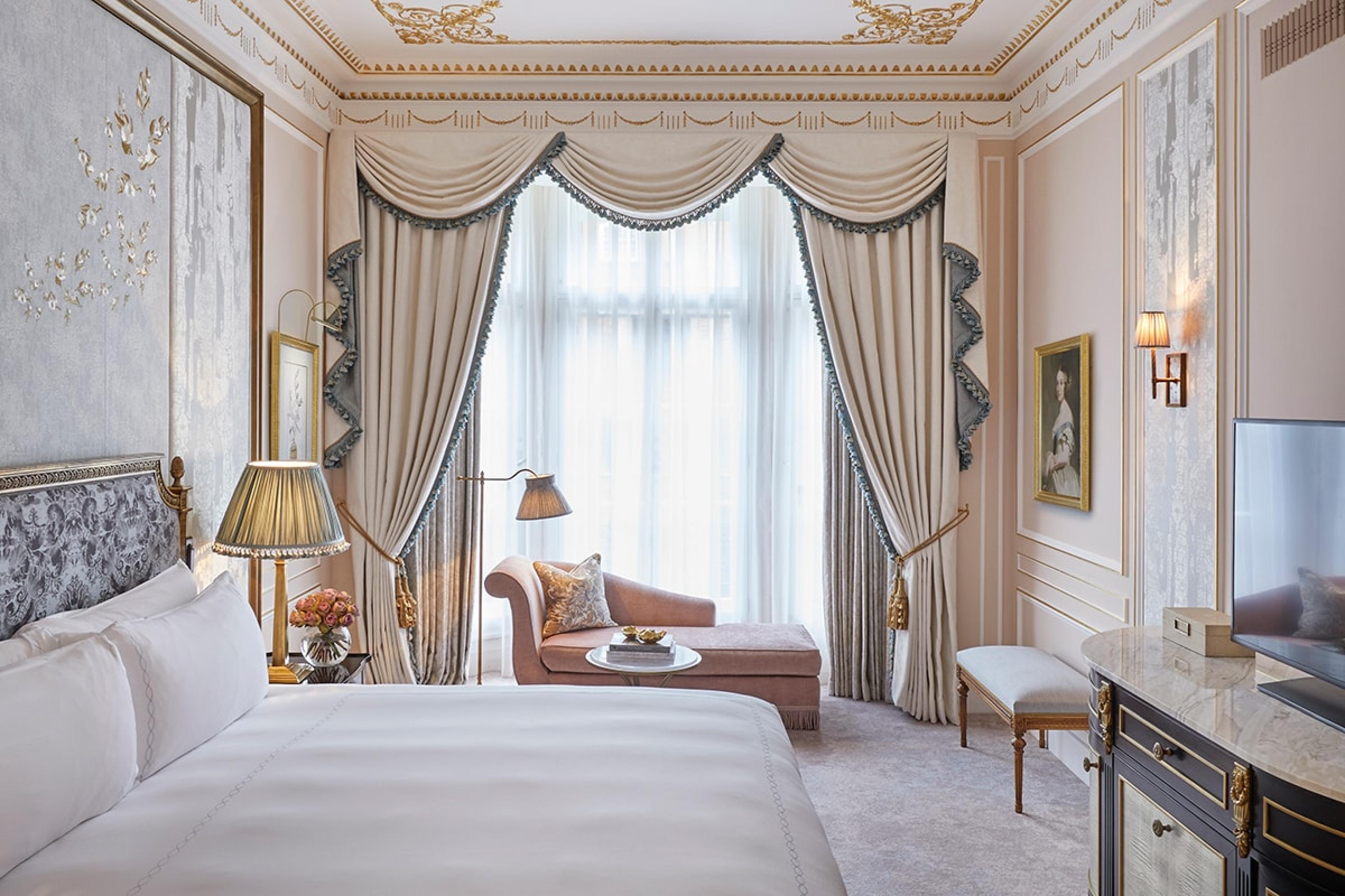 traditional and grand hotel room with scalloped white curtains and a chaise lounge by the window