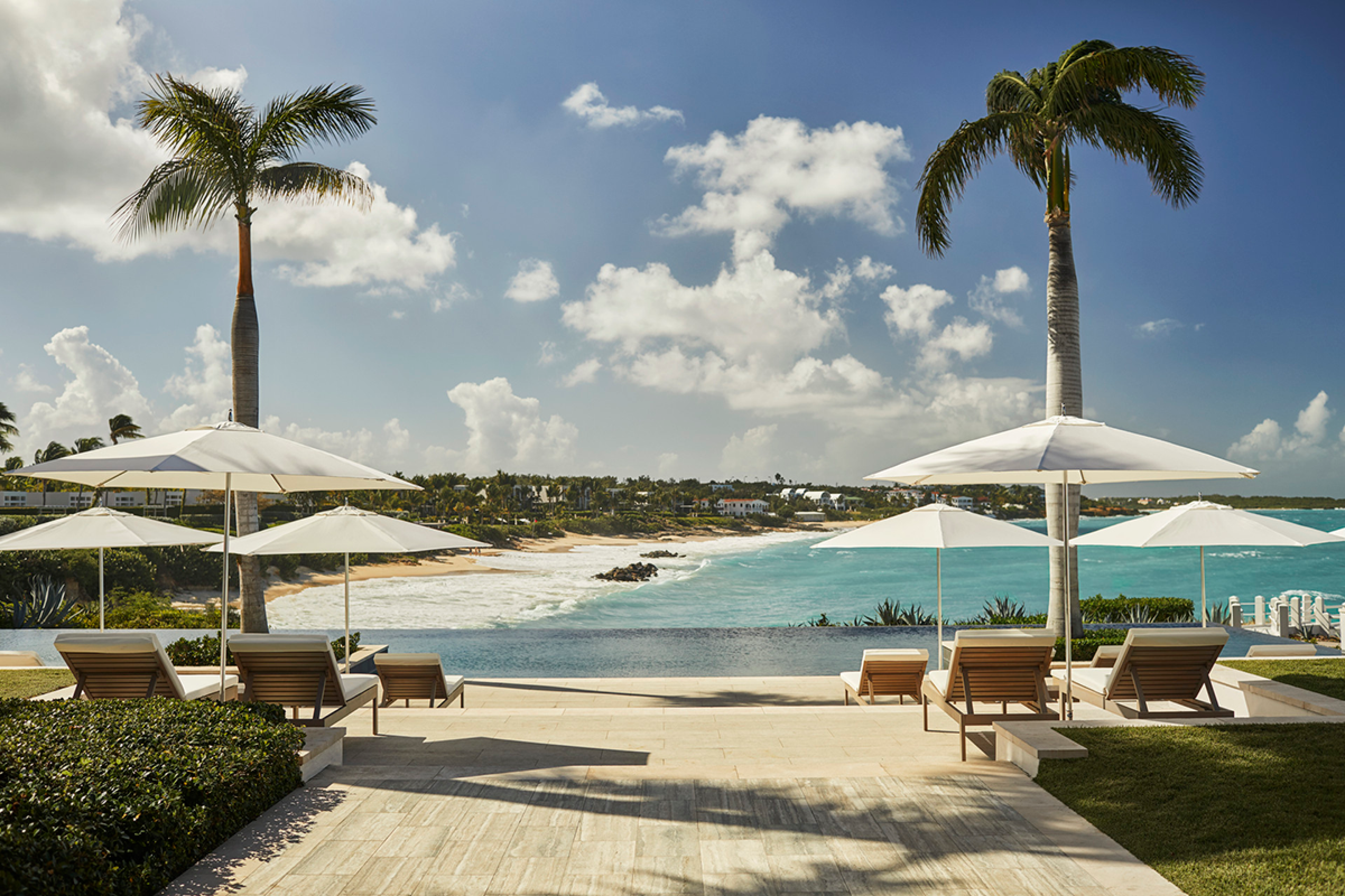 Pool deck with lounge chairs and white umbrellas overlooks the ocean