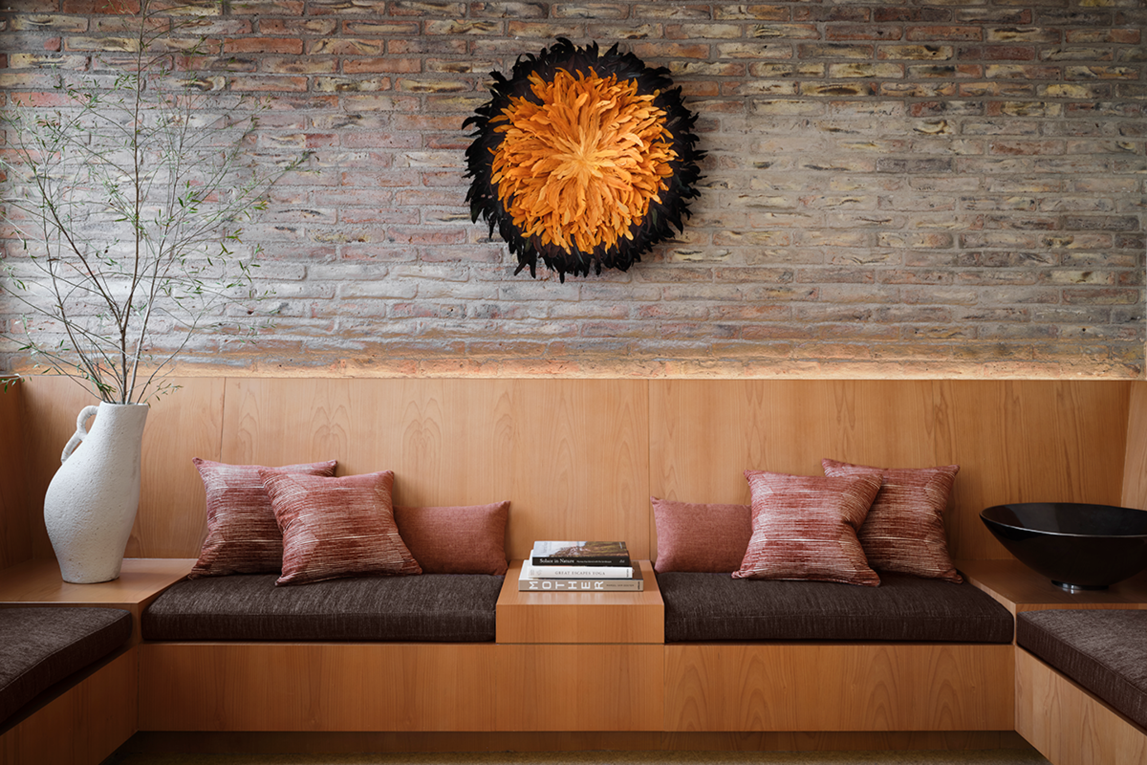wooden couches built into a wall with grey cushions and purple silk pillows. There are books and magazines out to read. The wall is stone with a large circular art hanging 