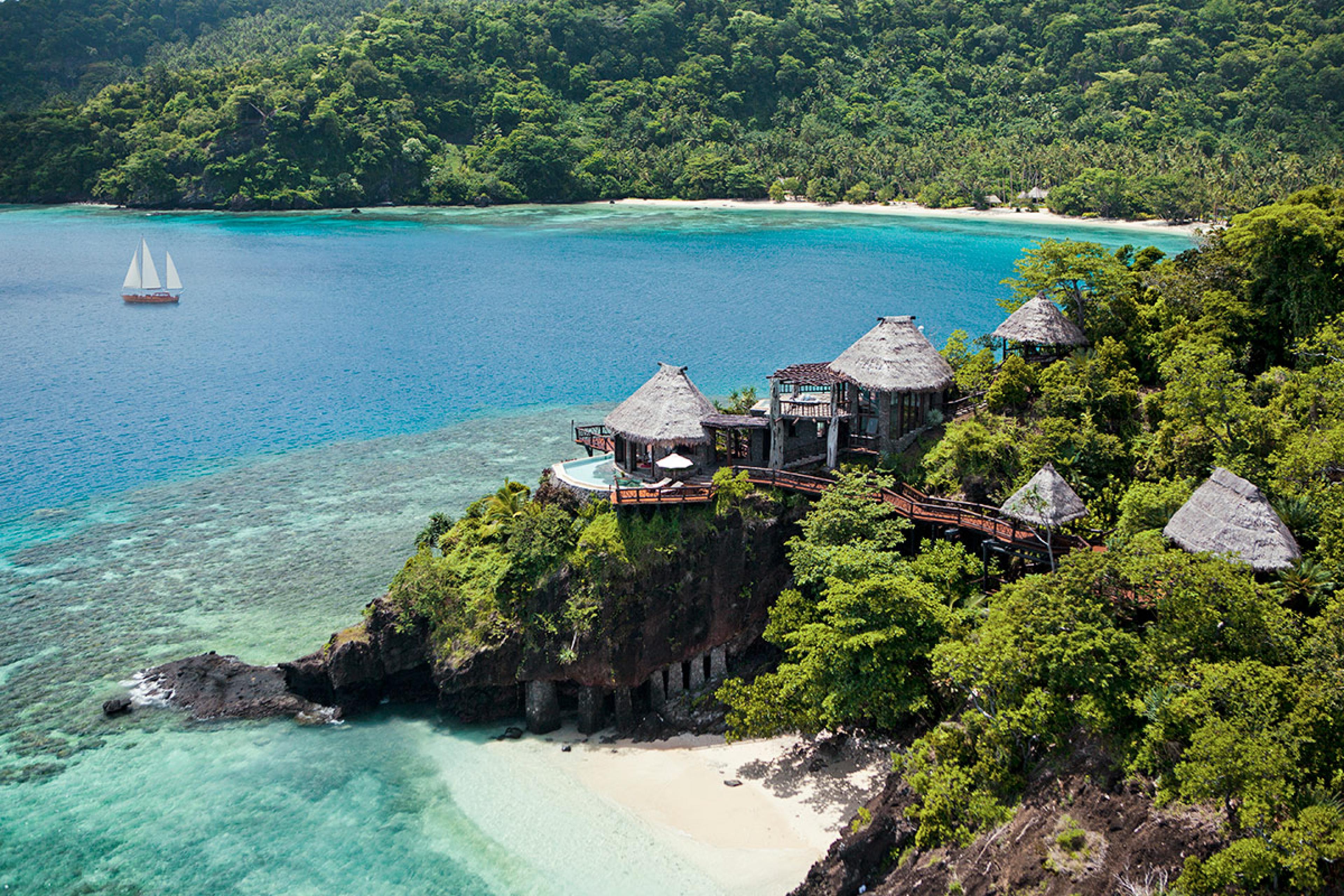 aerial view of coastal cliff above a beach on a tropical island with open-air thatch-roof luxury huts