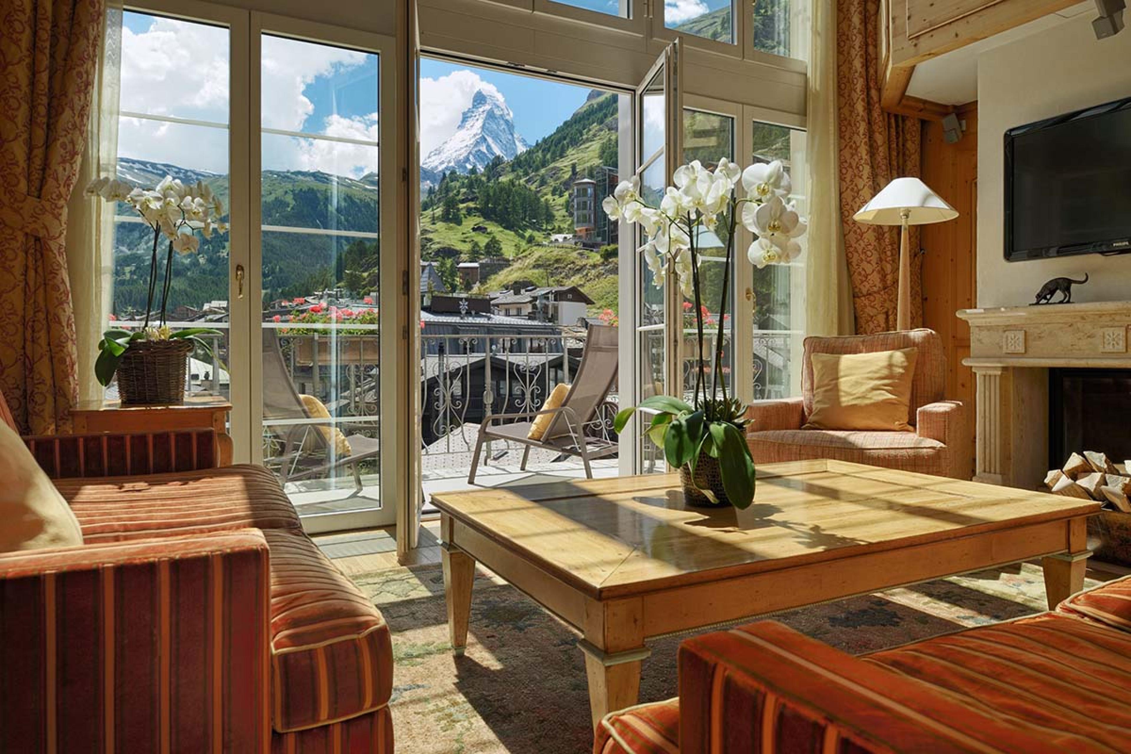 living room with a wooden table and glass doors open on a terrace with views of a jagged mountaintop