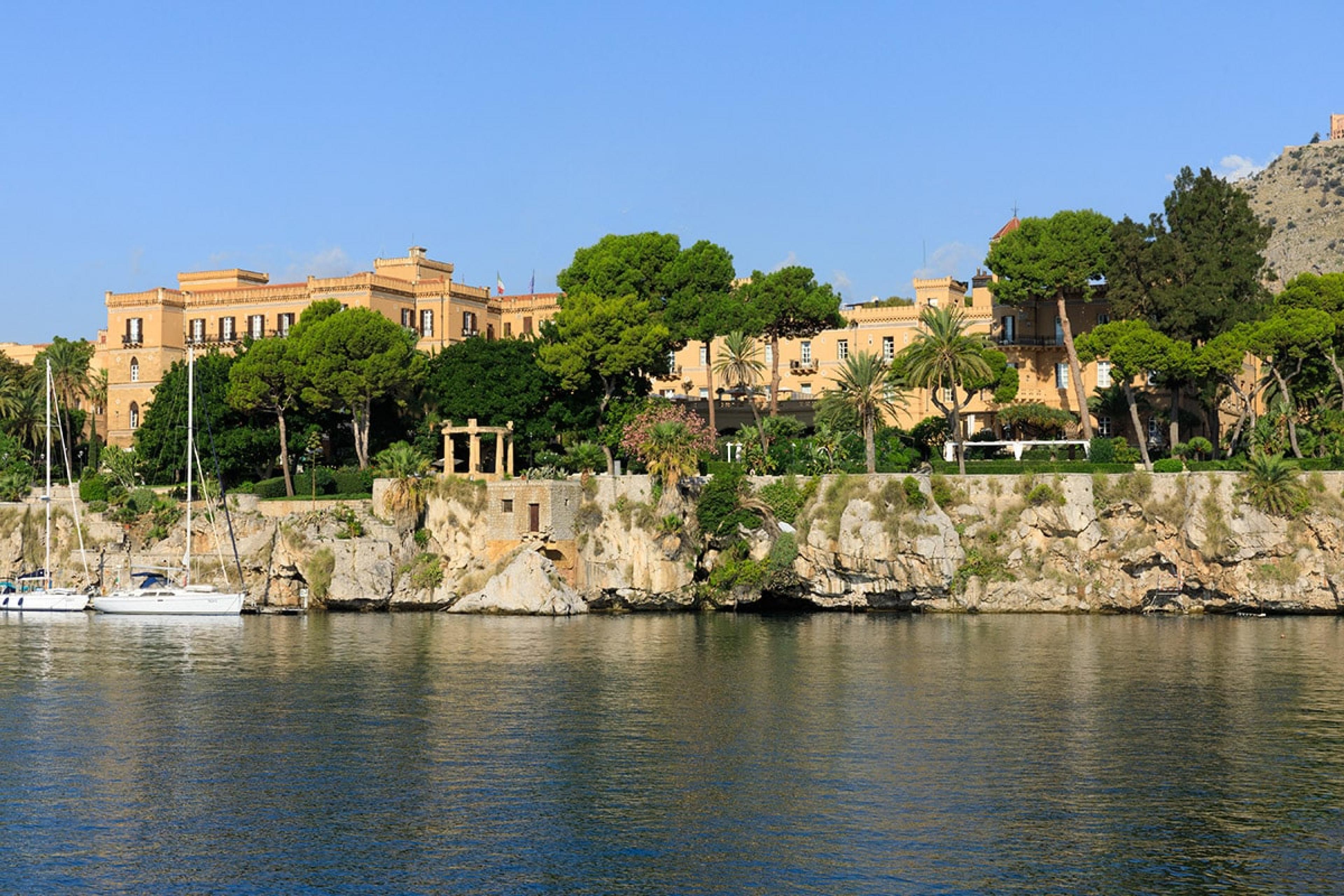 looking over water to italianate villa-style hotel buildings on a coastal cliff 