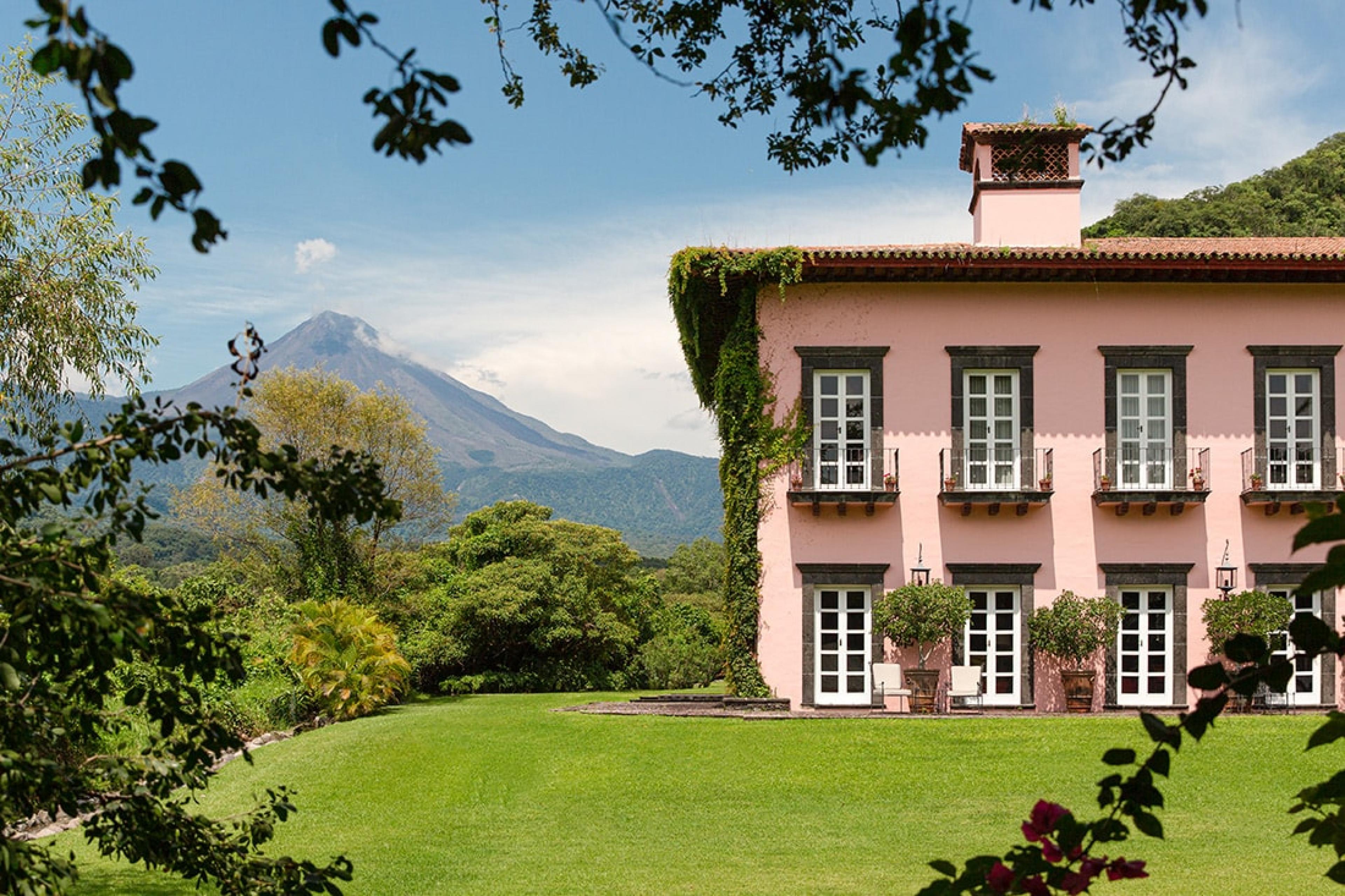 spanish colonial pink hacienda at top of lawn with volcano in the background