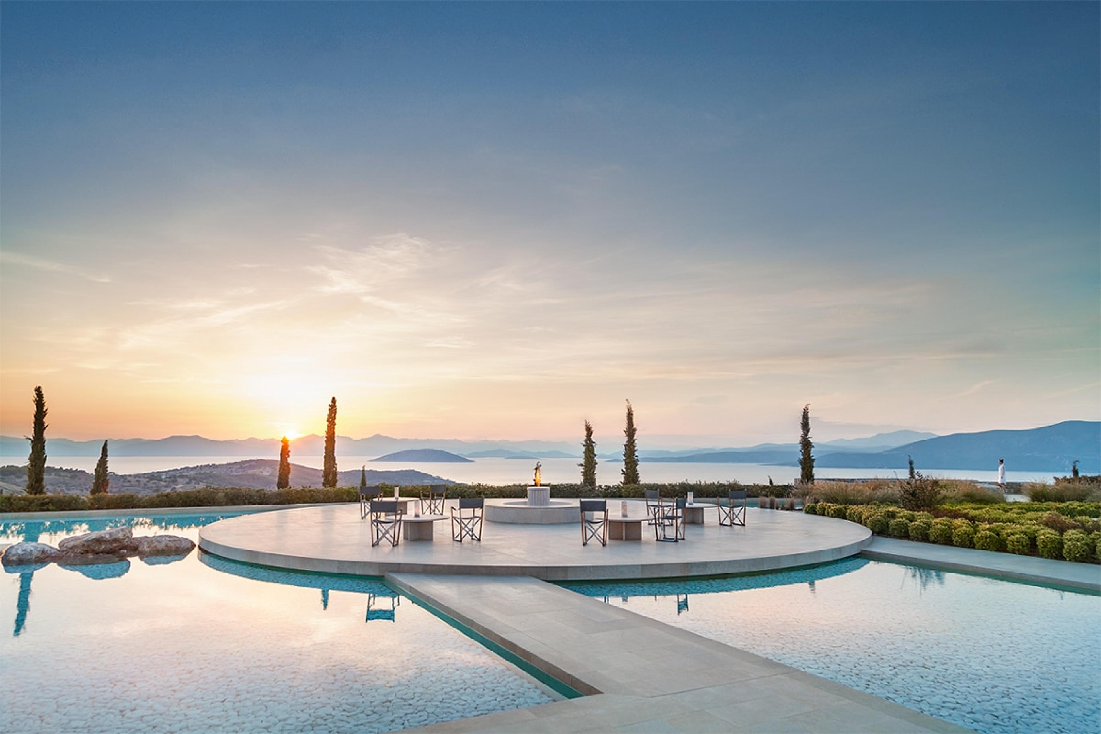view over terrace bisected by shallow pools on hilltop overlooking greek island view at sunset