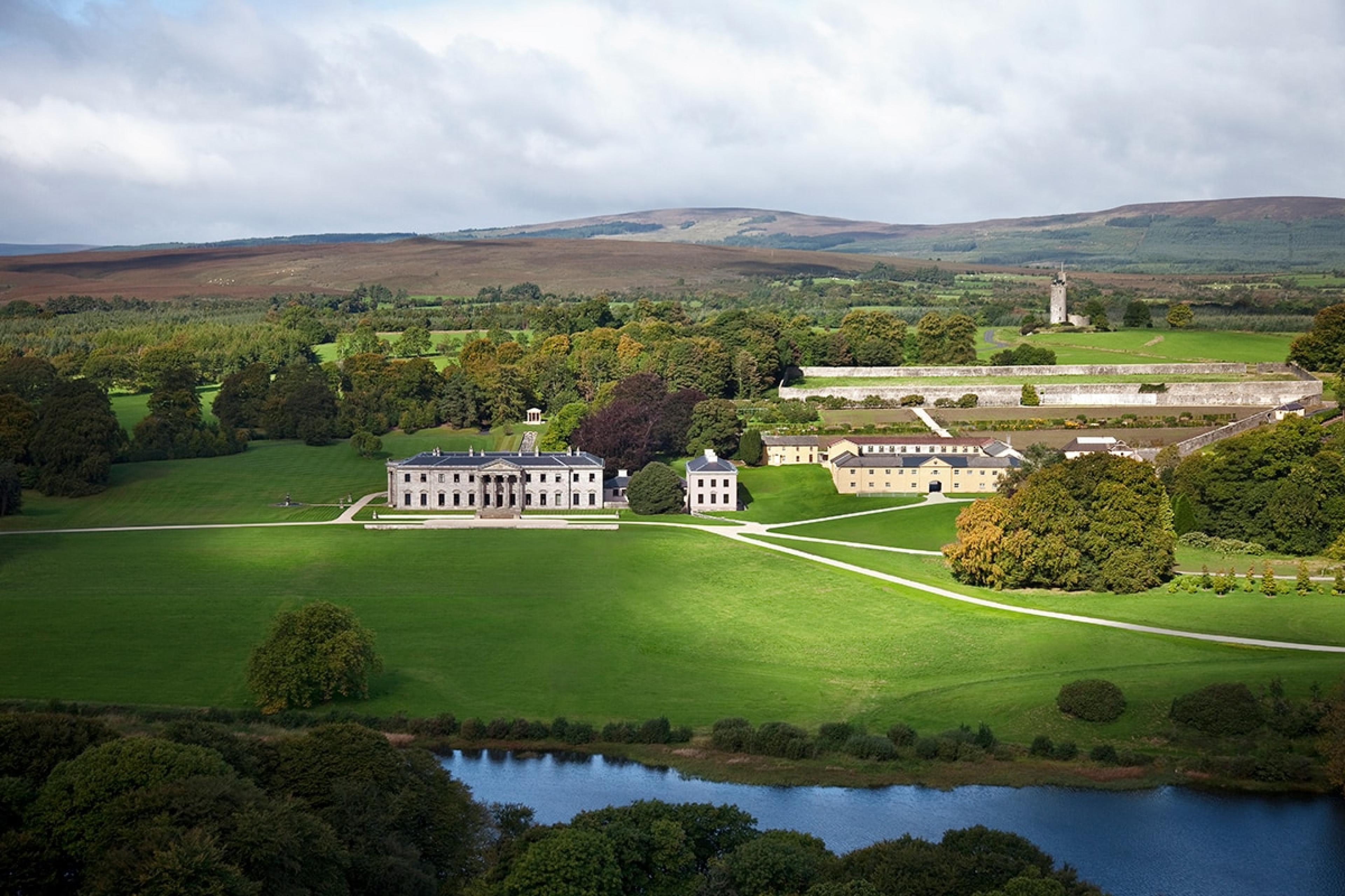aerial view of grand irish estate hotel with palace-like main building set back from a pond