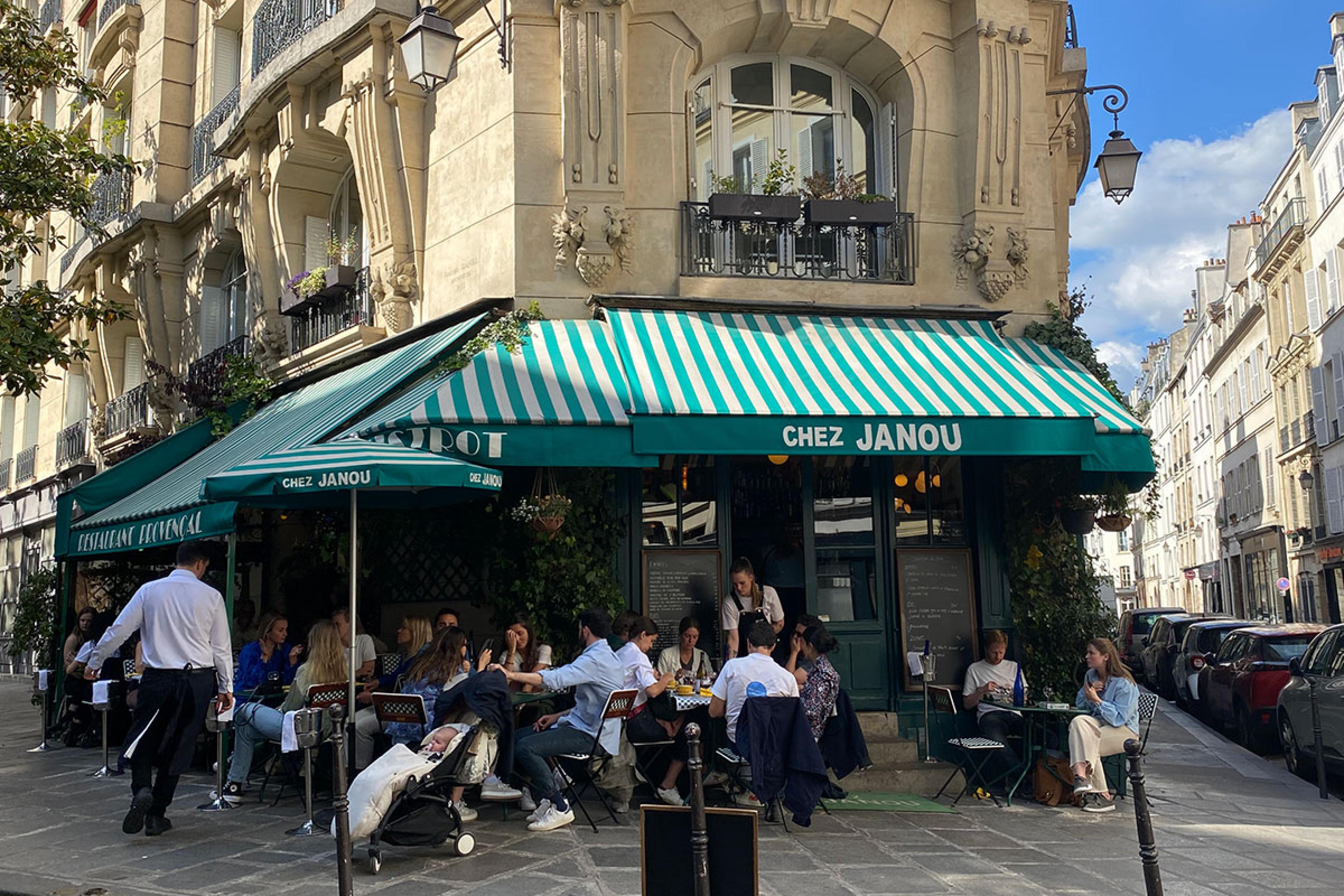 street cafe in paris on a corner with green awning reading chez janou