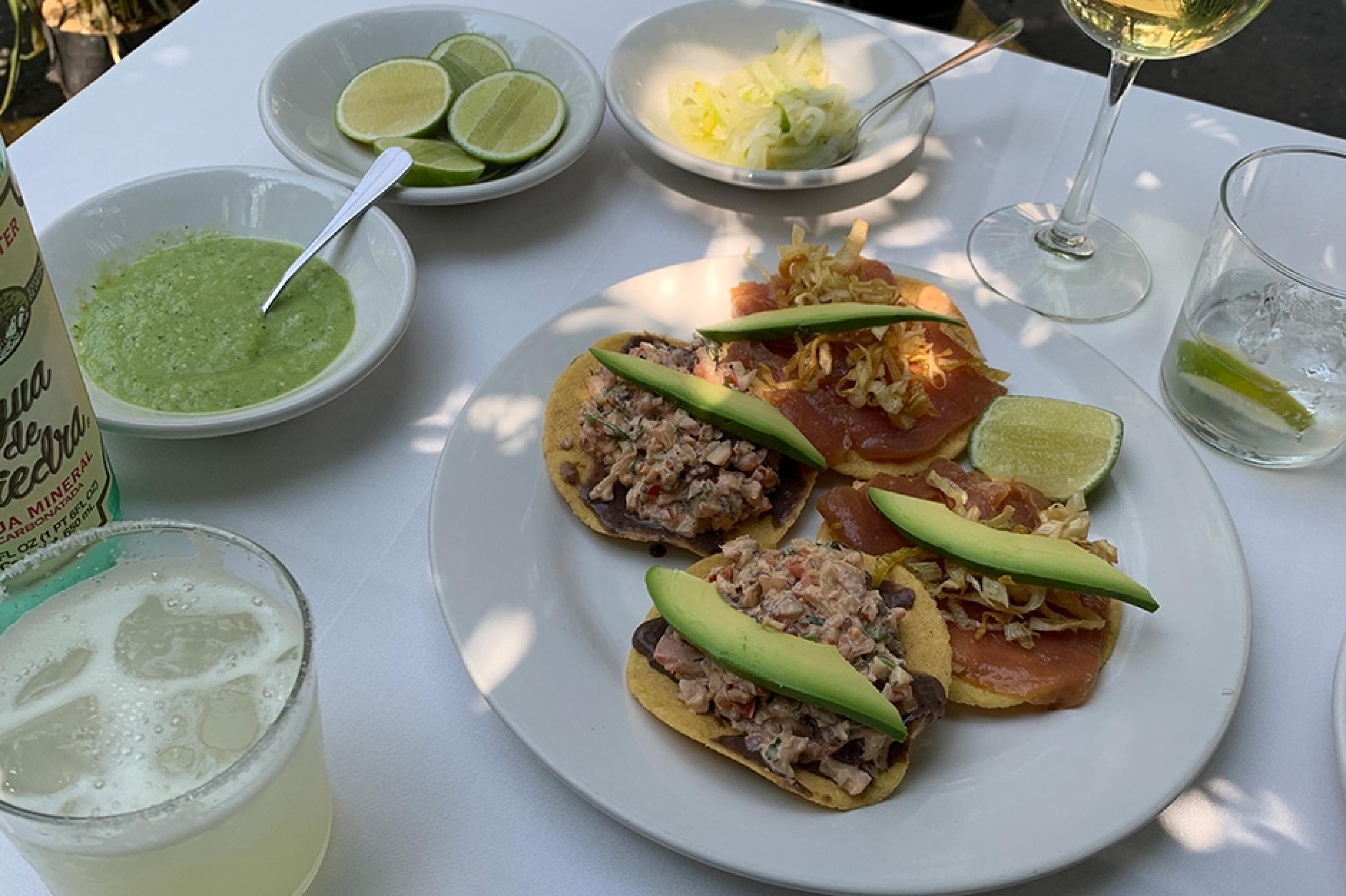 four tacos on a plate with a margarita to the left at a restaurant in mexico city