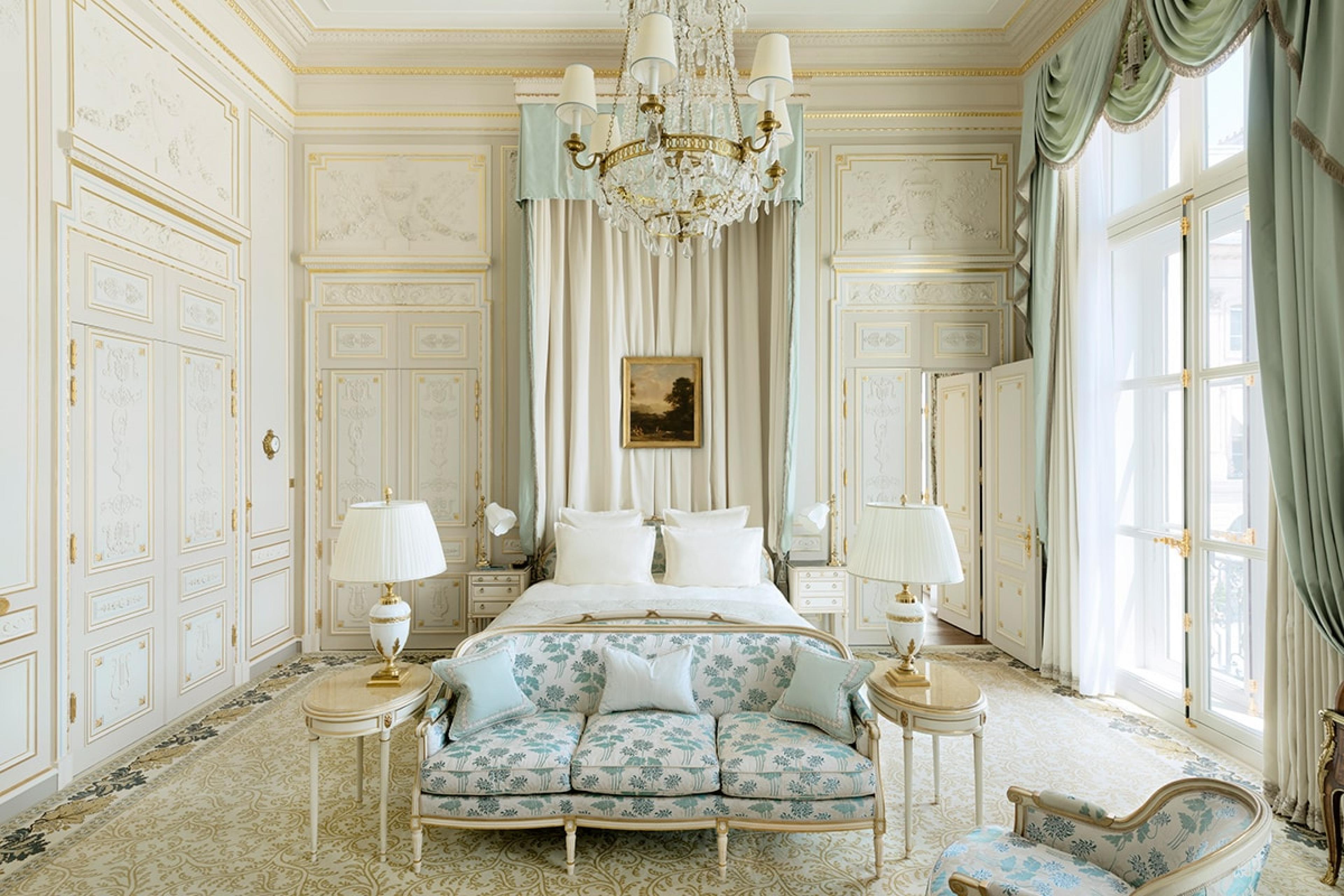 grand hotel suite in paris with tall ceilings and a chandelier and a canopy bed and white walls with blue fabric accents