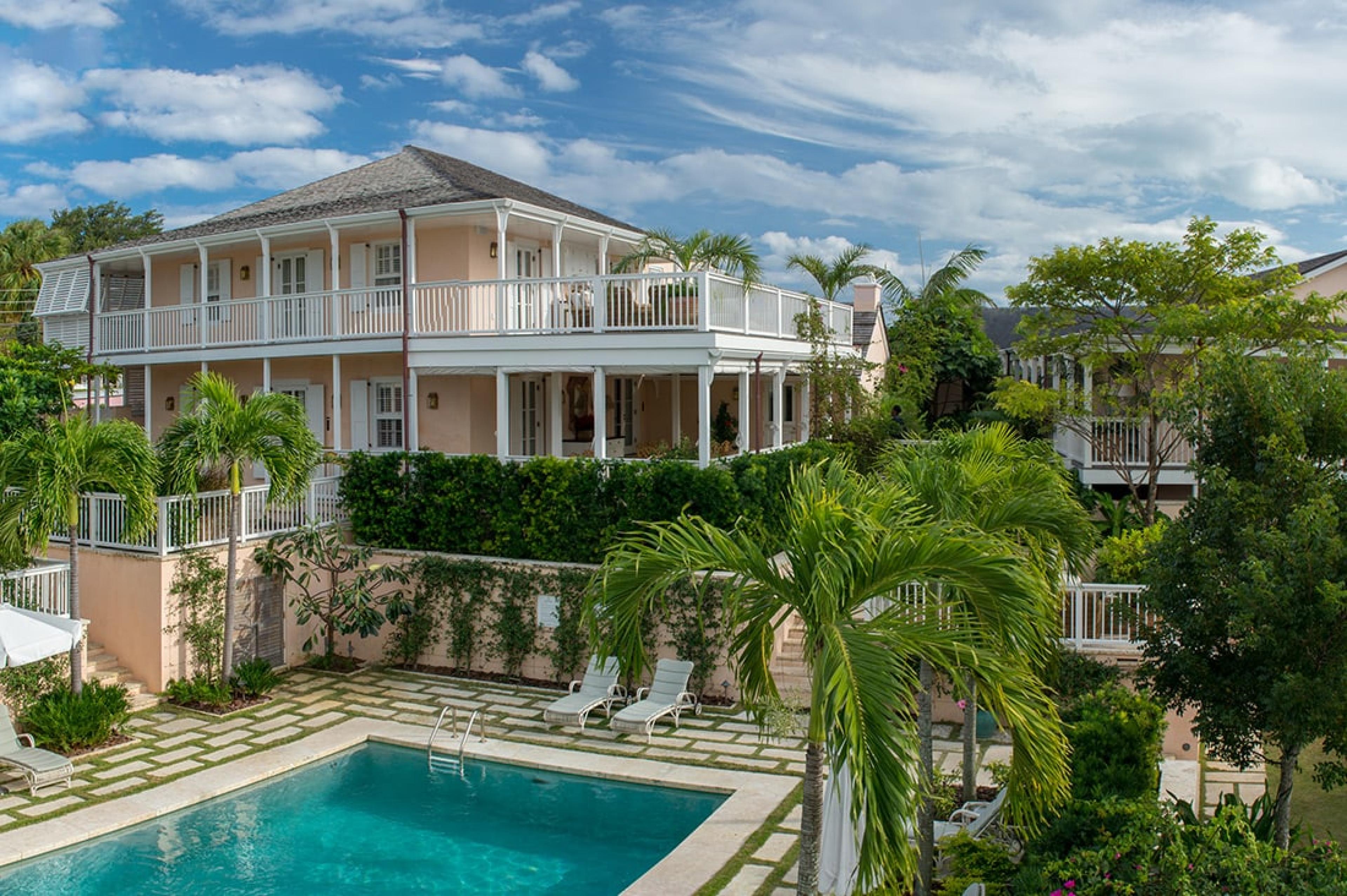 view from above of a pool and surround stone deck with pink building and palm trees in background