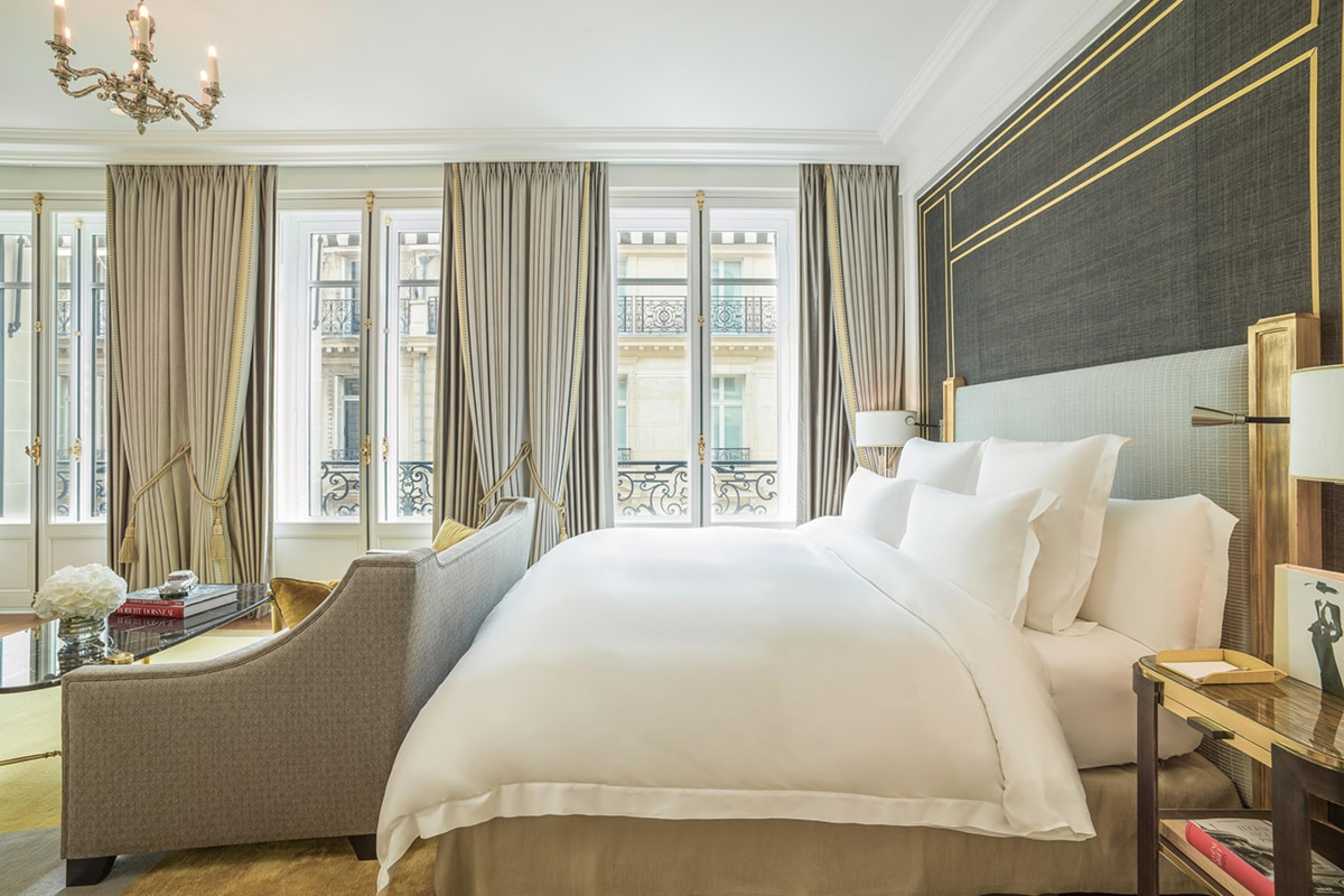 hotel room with white linens and gray headboard and windows looking out to paris buildings across street