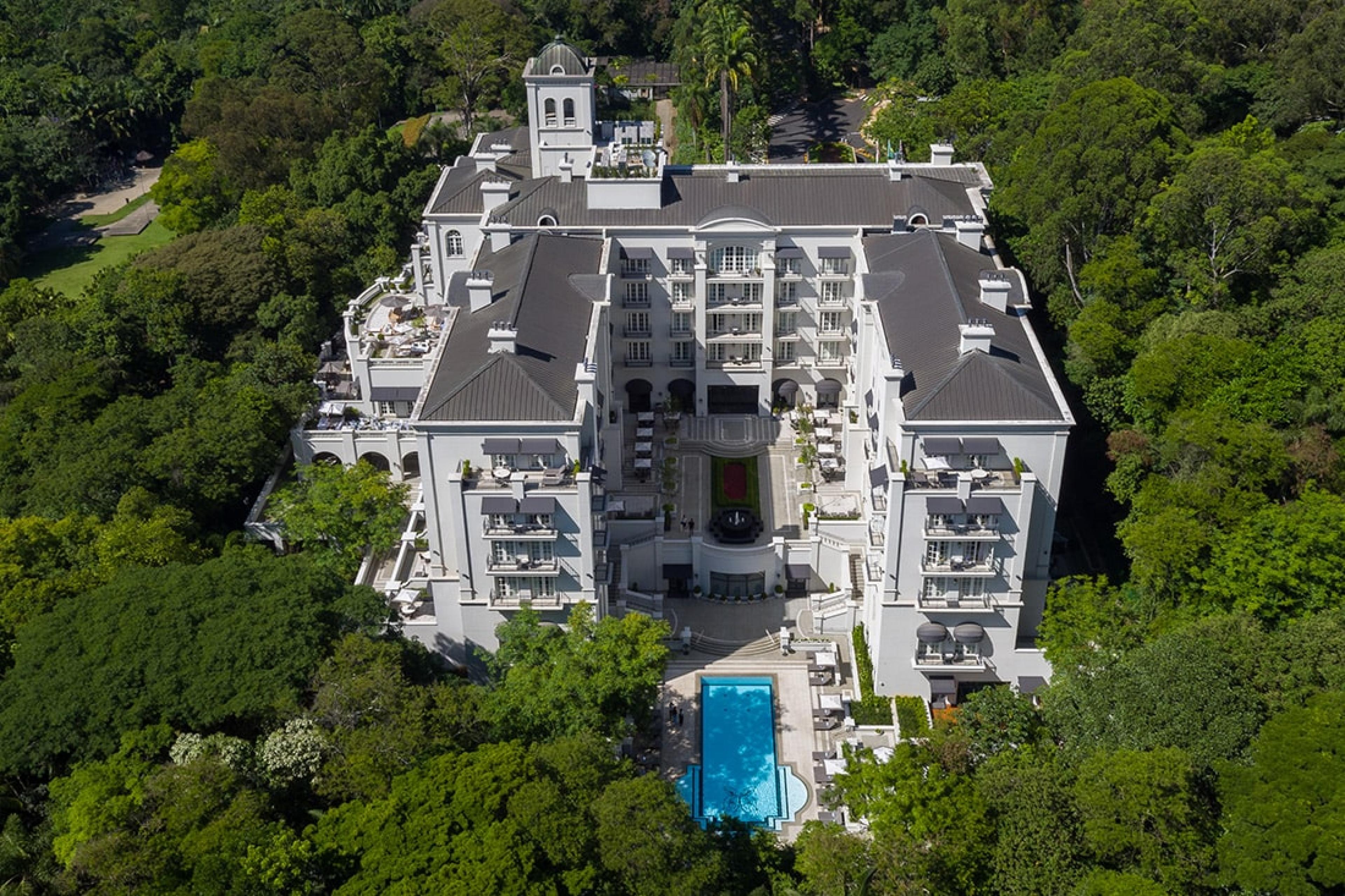 aerial view of U-shaped large hotel with pool in center courtyard and surrounded by dense trees