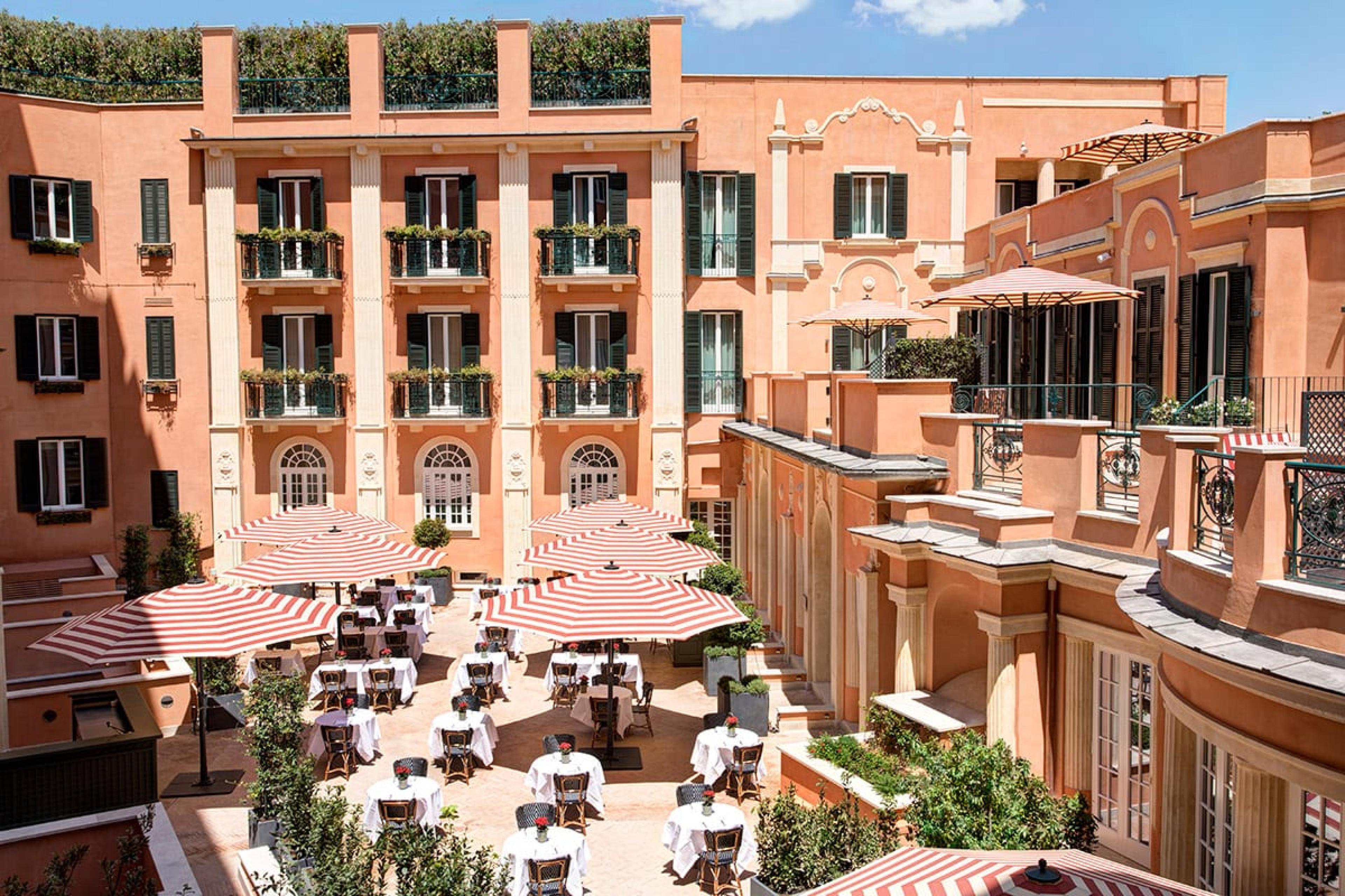 courtyard of grand hotel in rome with lots of restaurant seating and hotel balconies above it