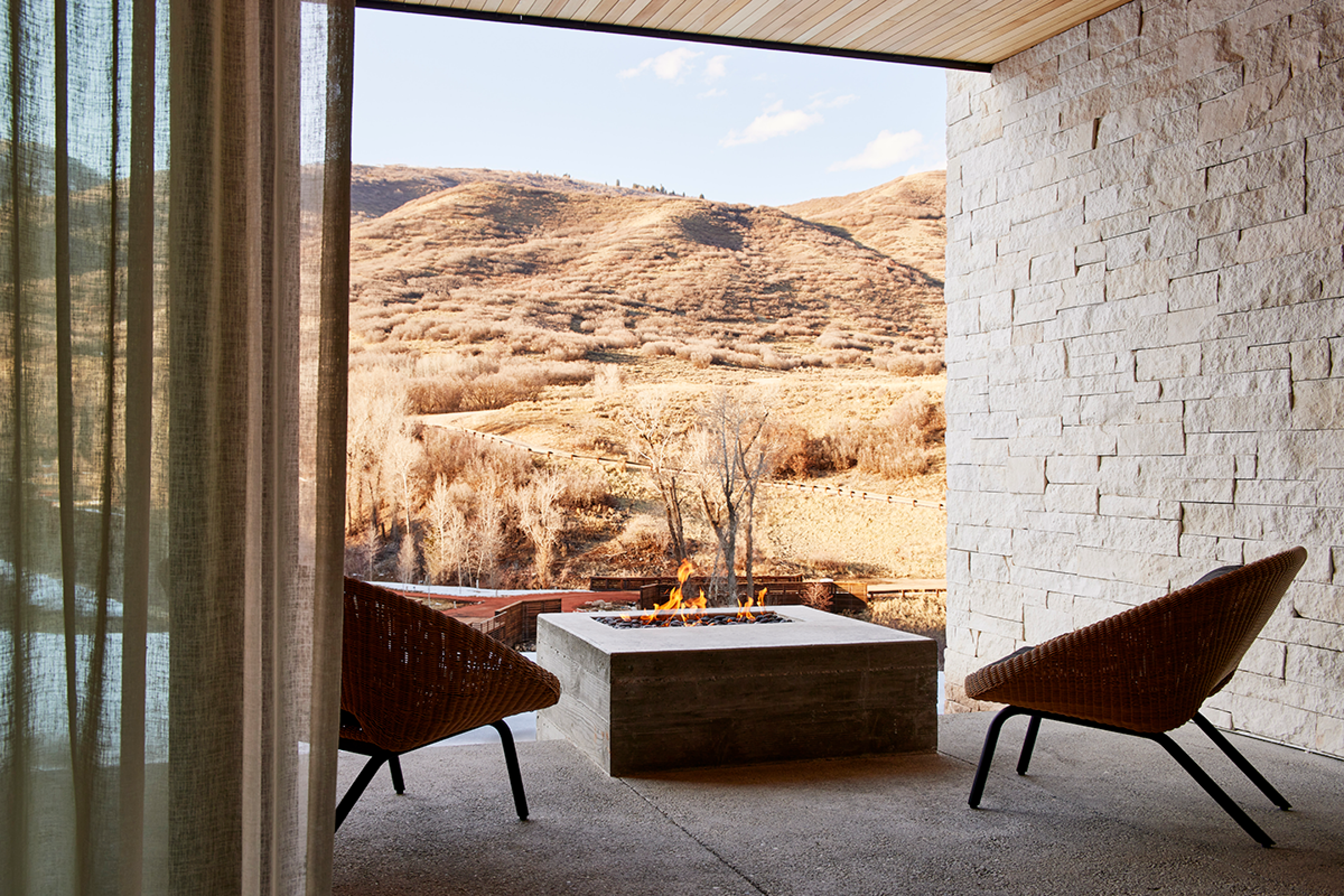 two chairs are on a patio with square stone firepit. Overlooks mountain landscape 