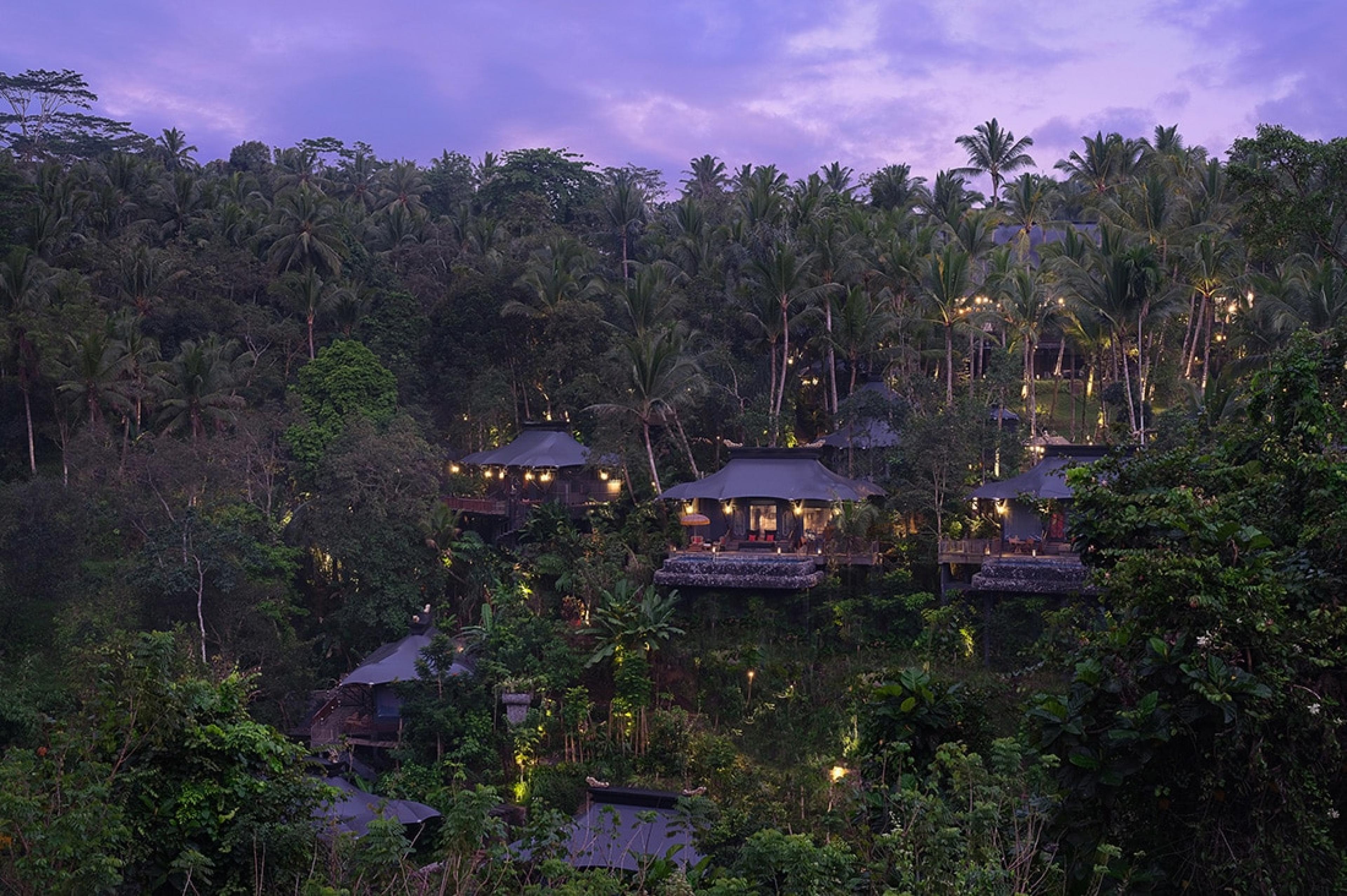 view across jungle valley to hotel made up of tented suites at dusk