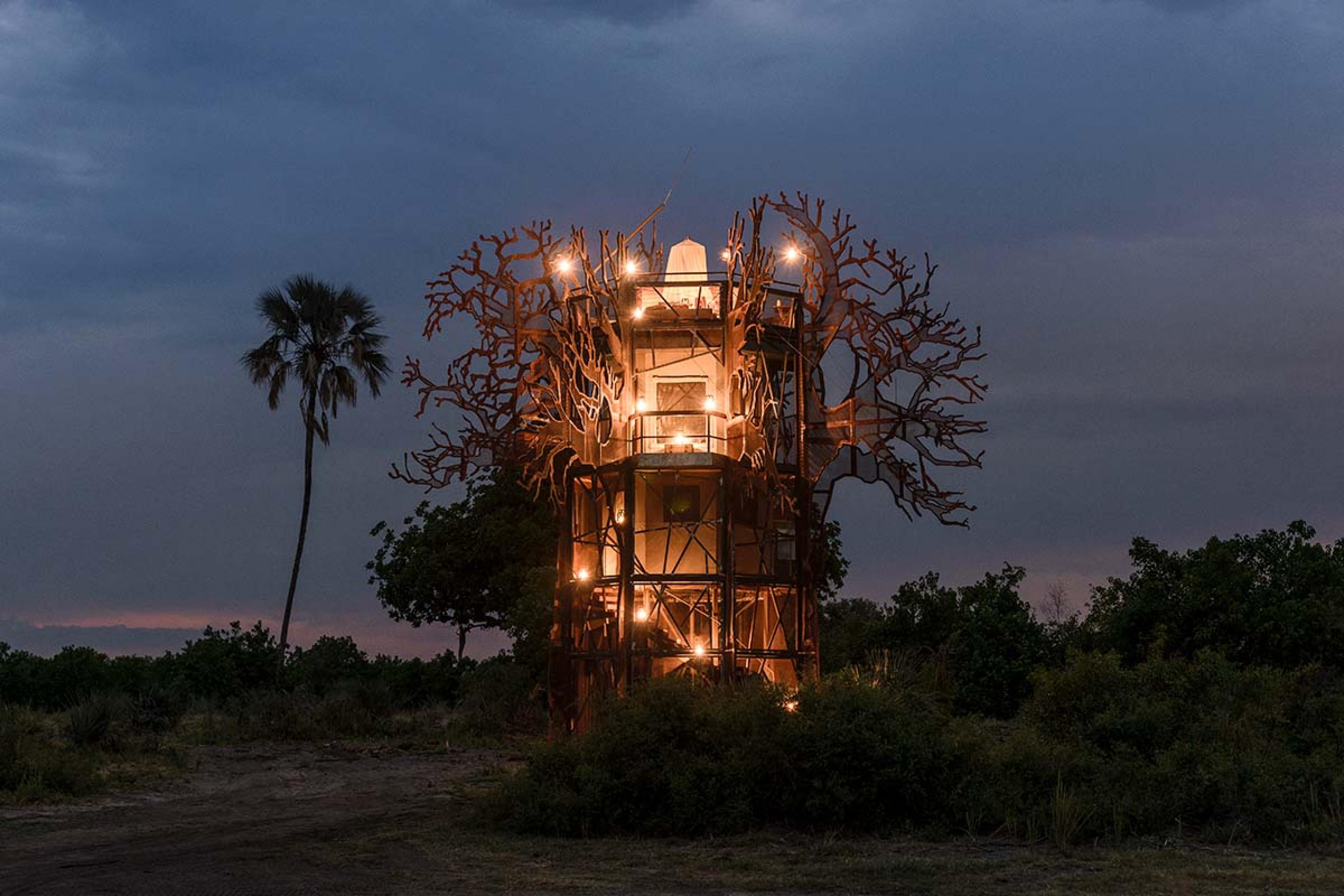 tall lit up villa structure with branches at night