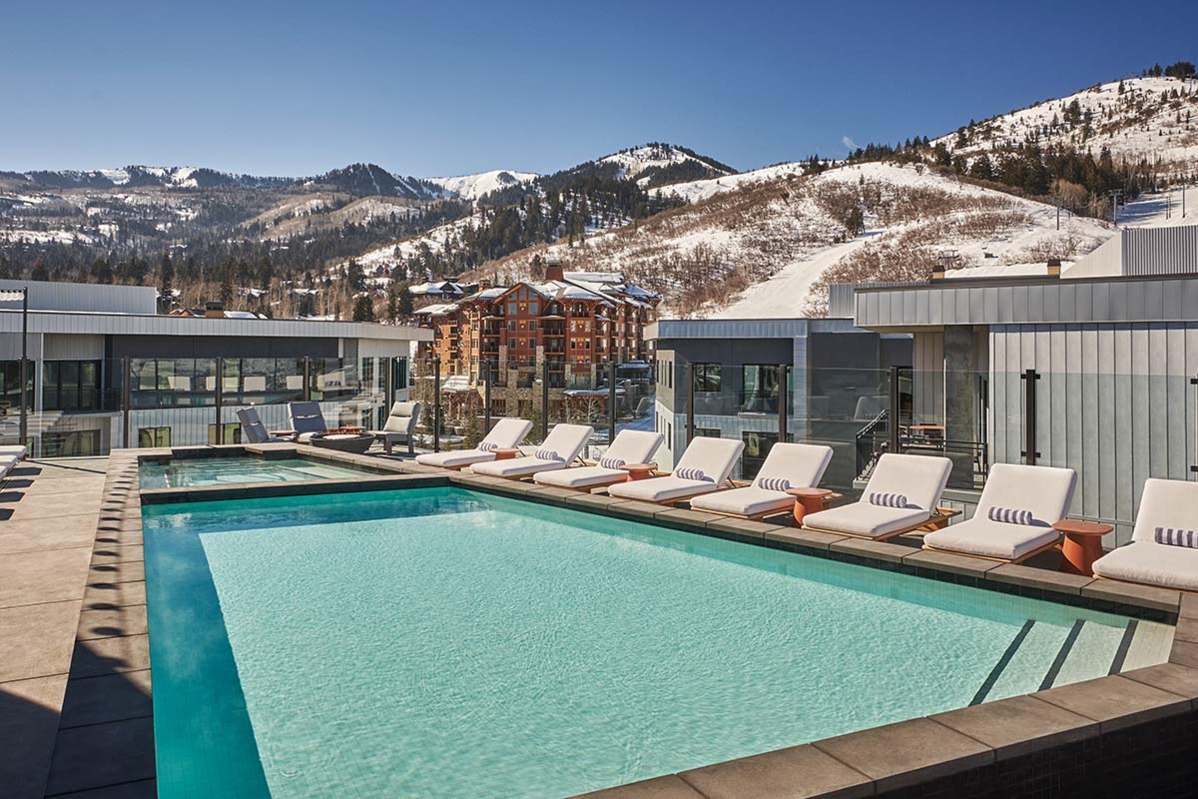 pool and hot tub lined with wide chairs looking out on snowy mountains