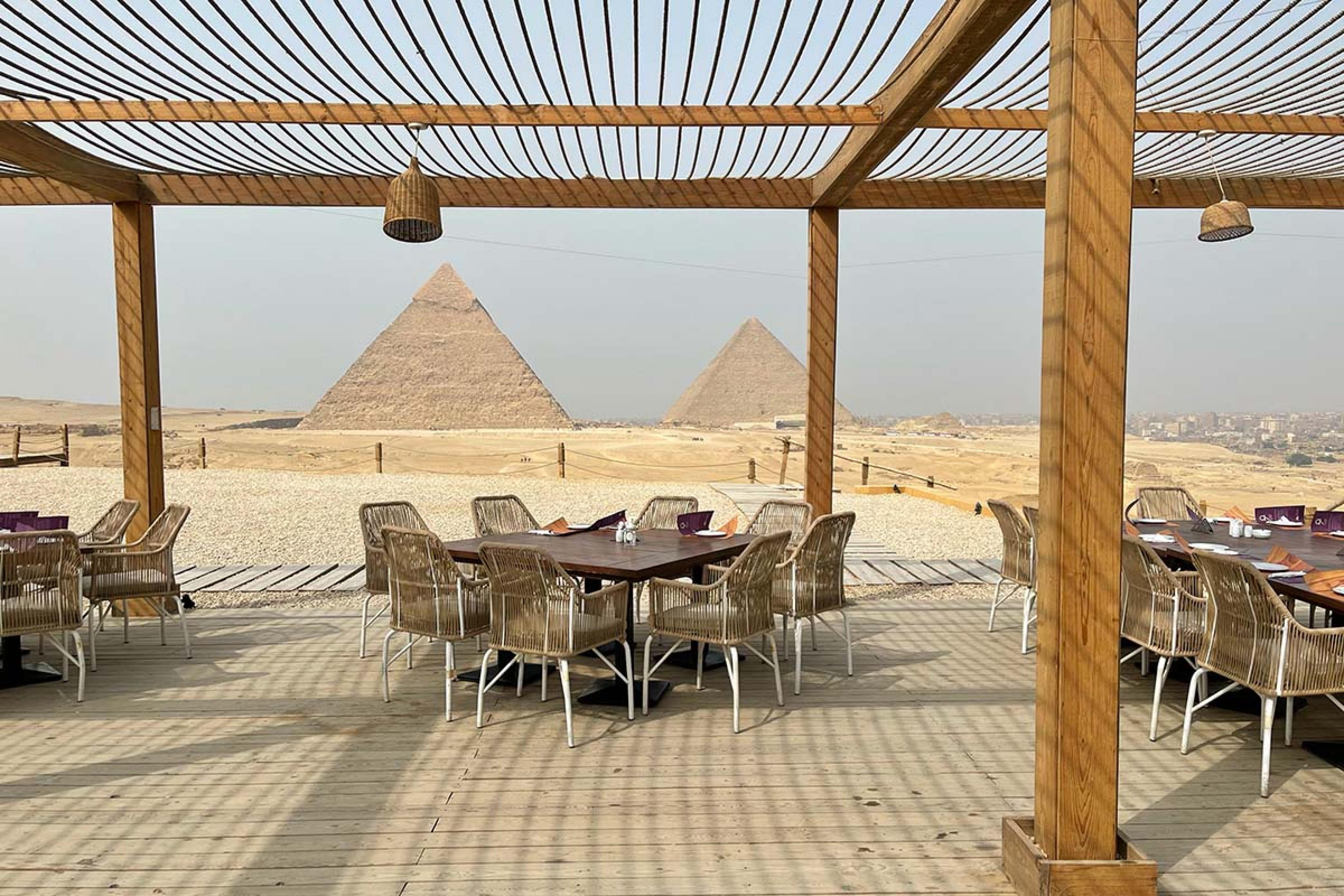 dining tables beneath a wooden structure with the pyramids in the background