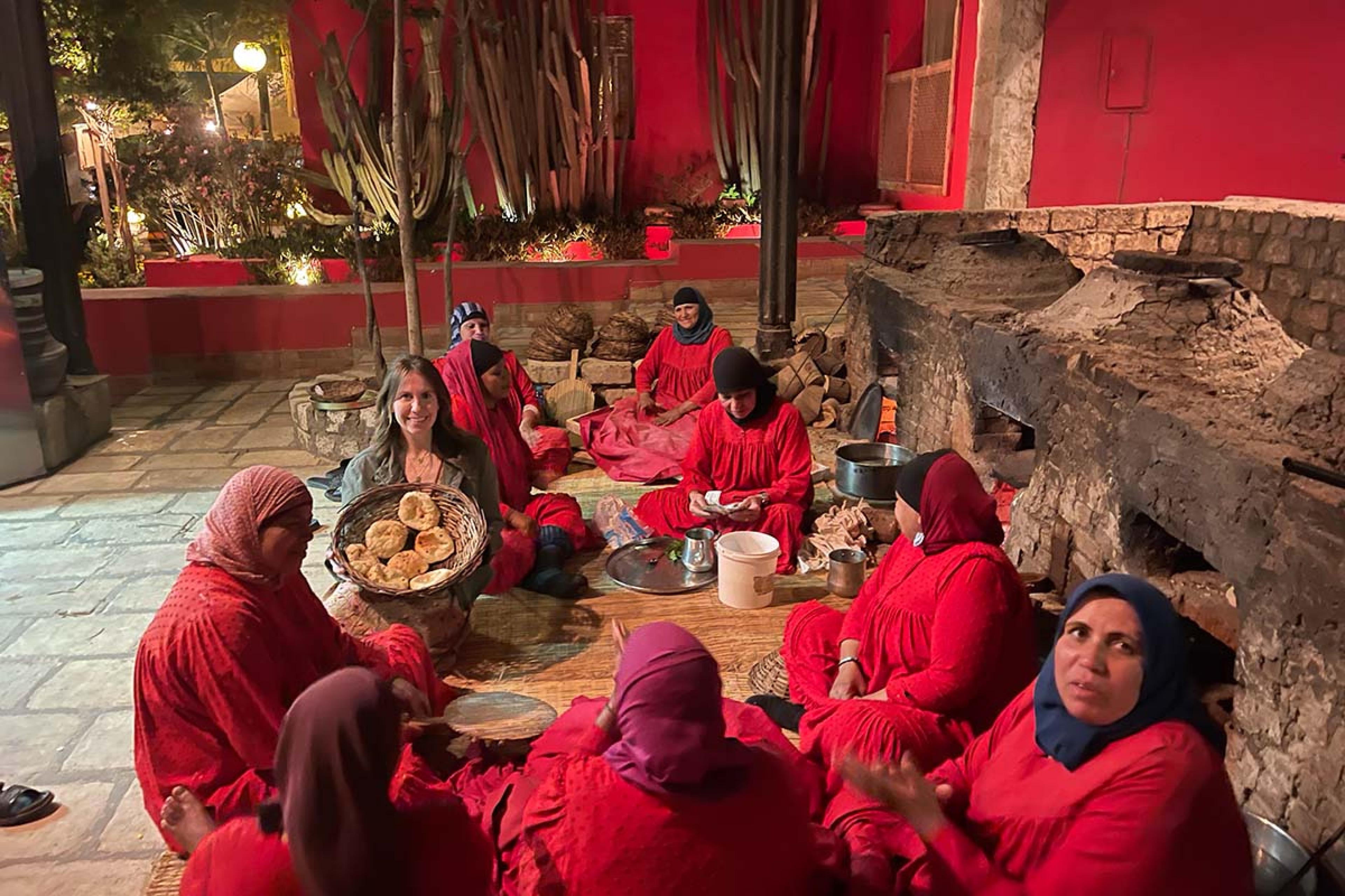 people dressed in red seated on a woven rug eating