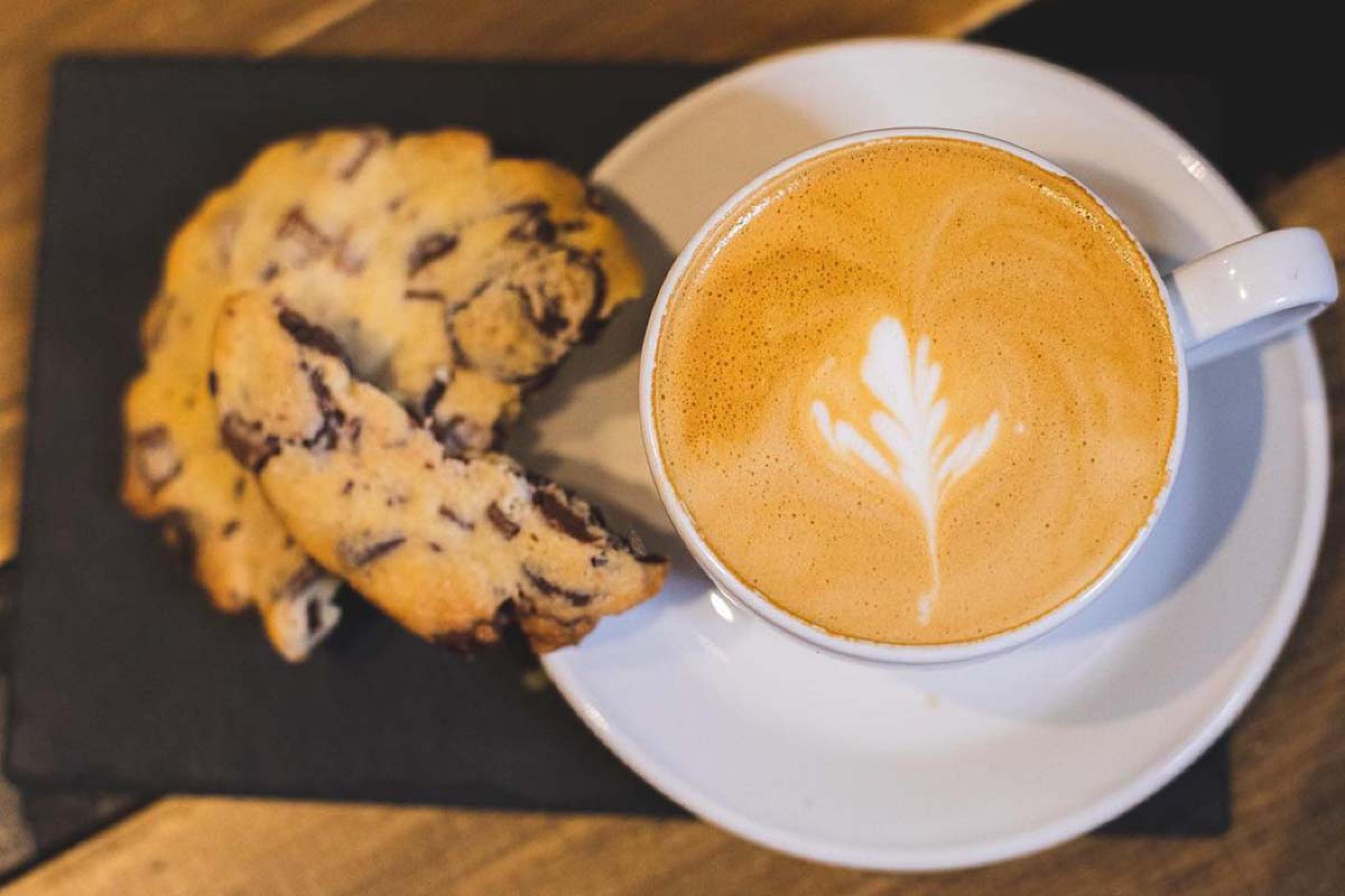 cappucino with a leaf design and a chocolate chip cookie
