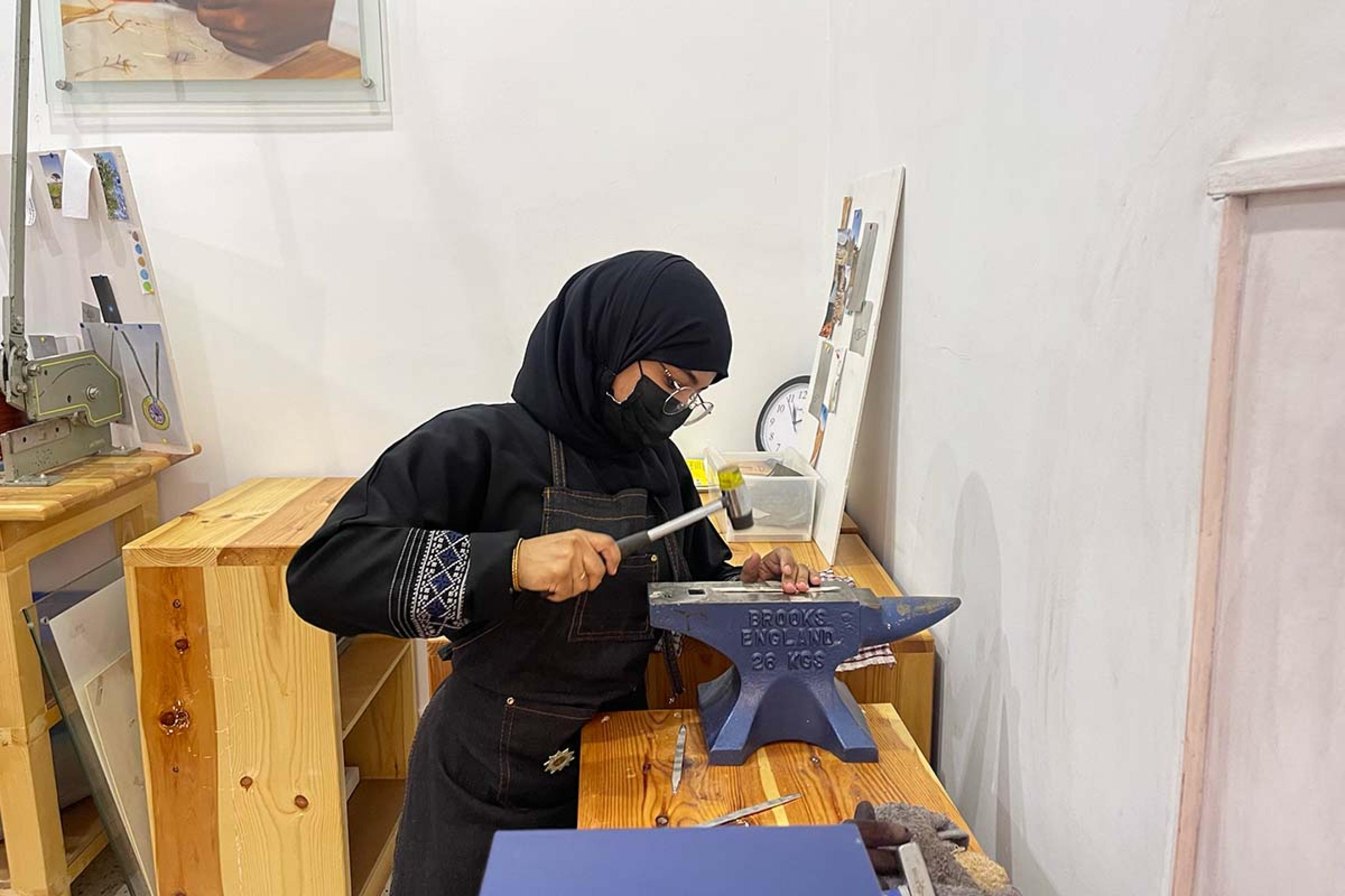 woman in an abaya crafting at a wooden table