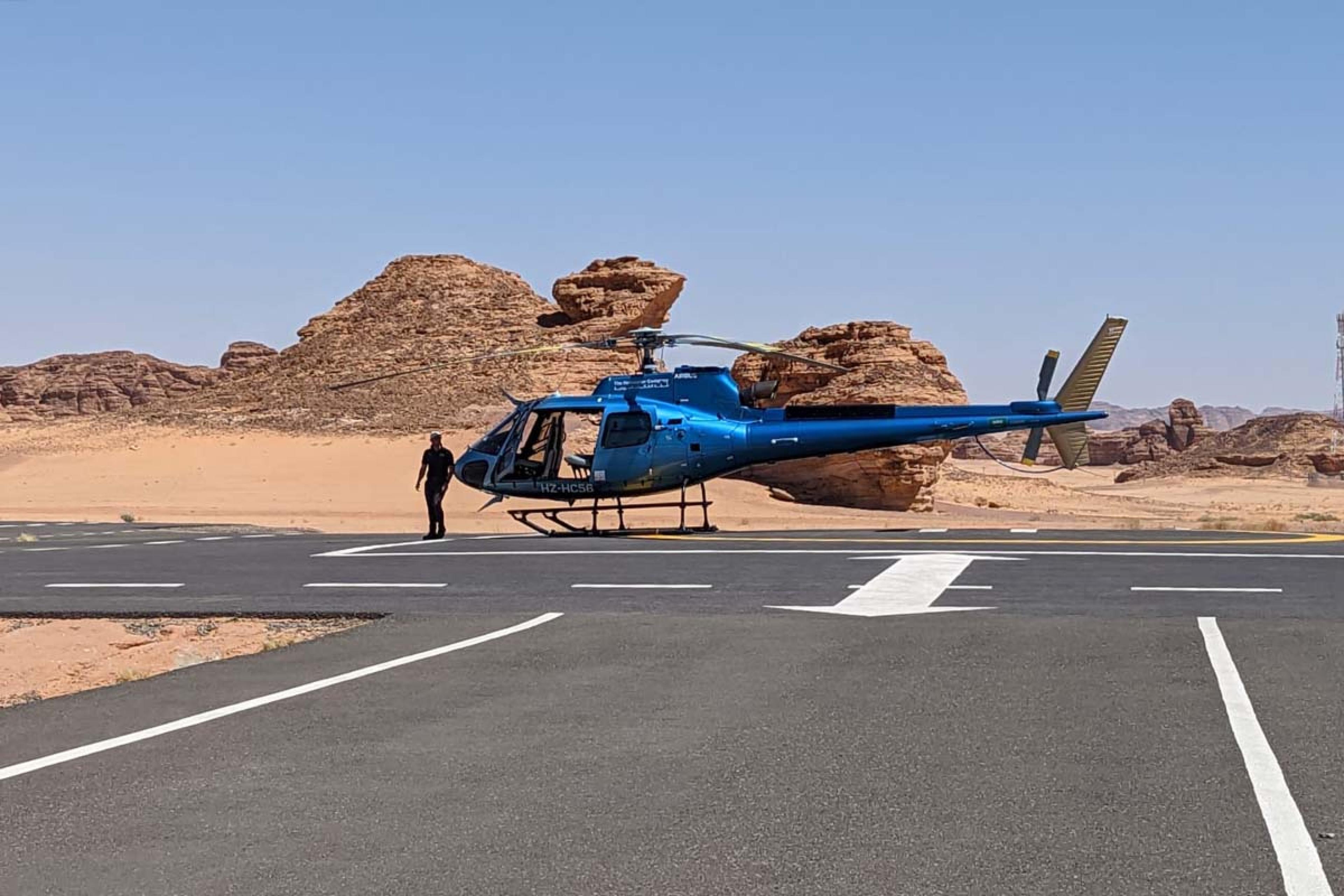 blue helicopter on a landing pad with a desert behind them