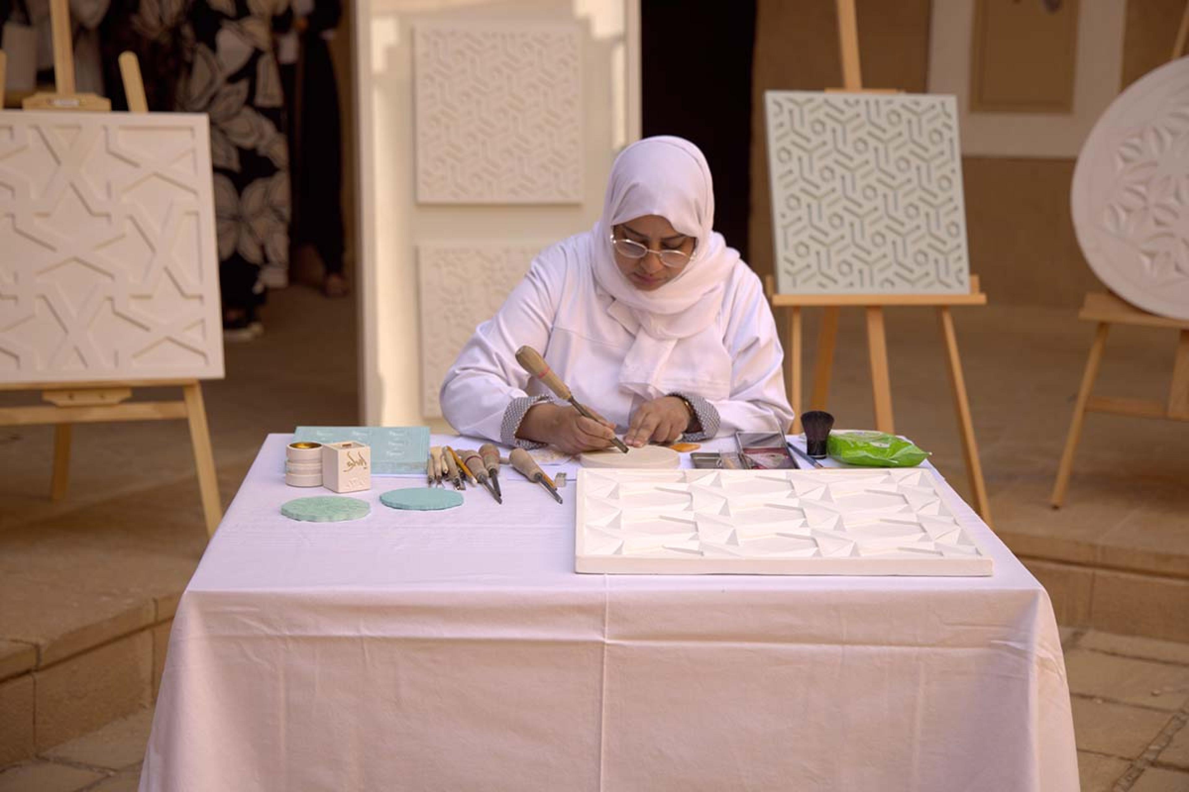 woman in a white abaya at a white table designing crafts