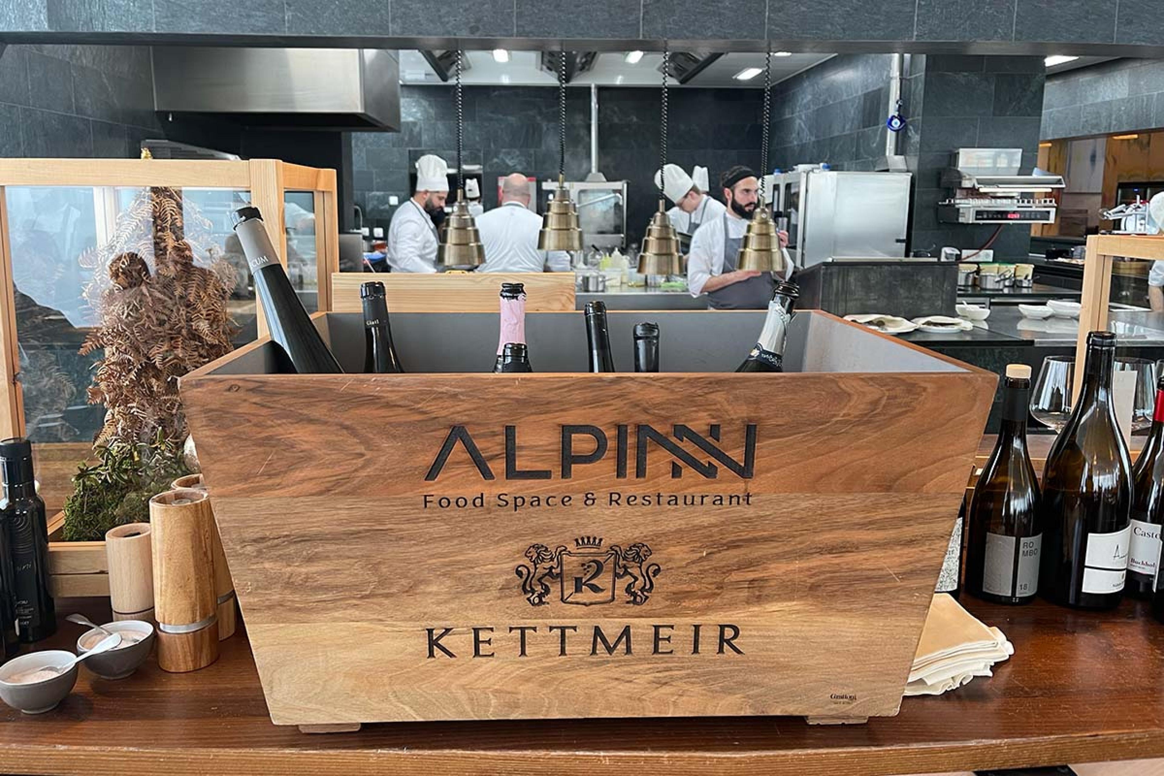 wooden box of wine with "AlpiNN" written on it and chefs in the background