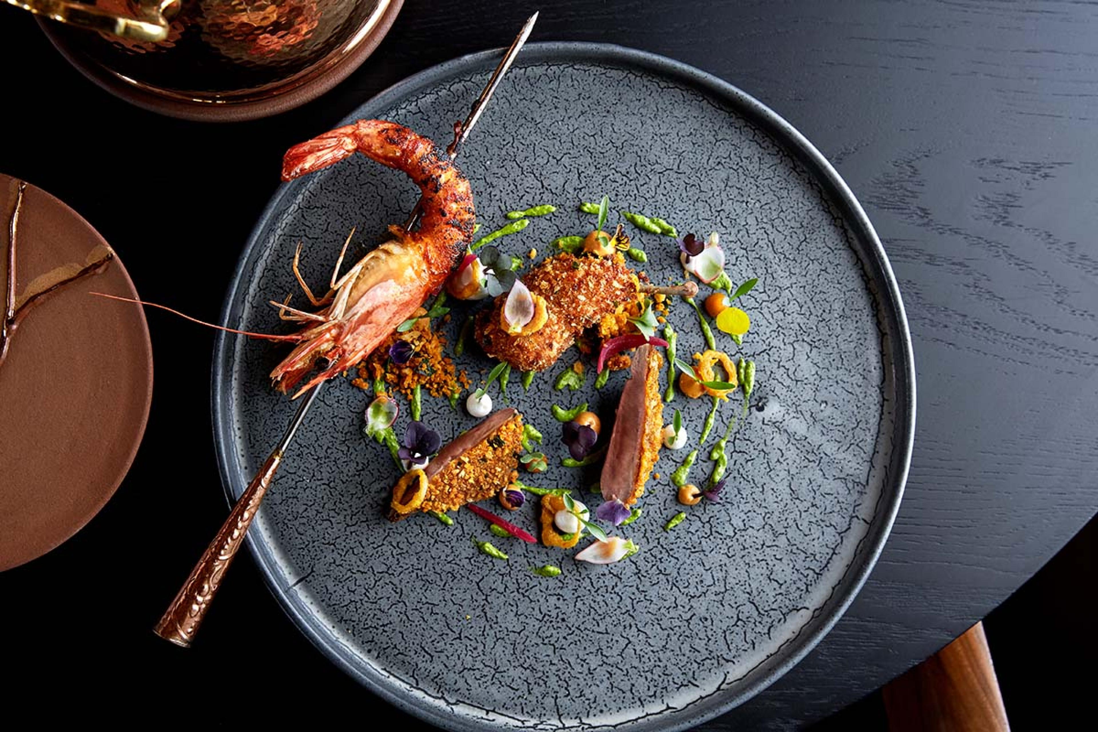 gray stone plate with seafood and a skewered crayfish