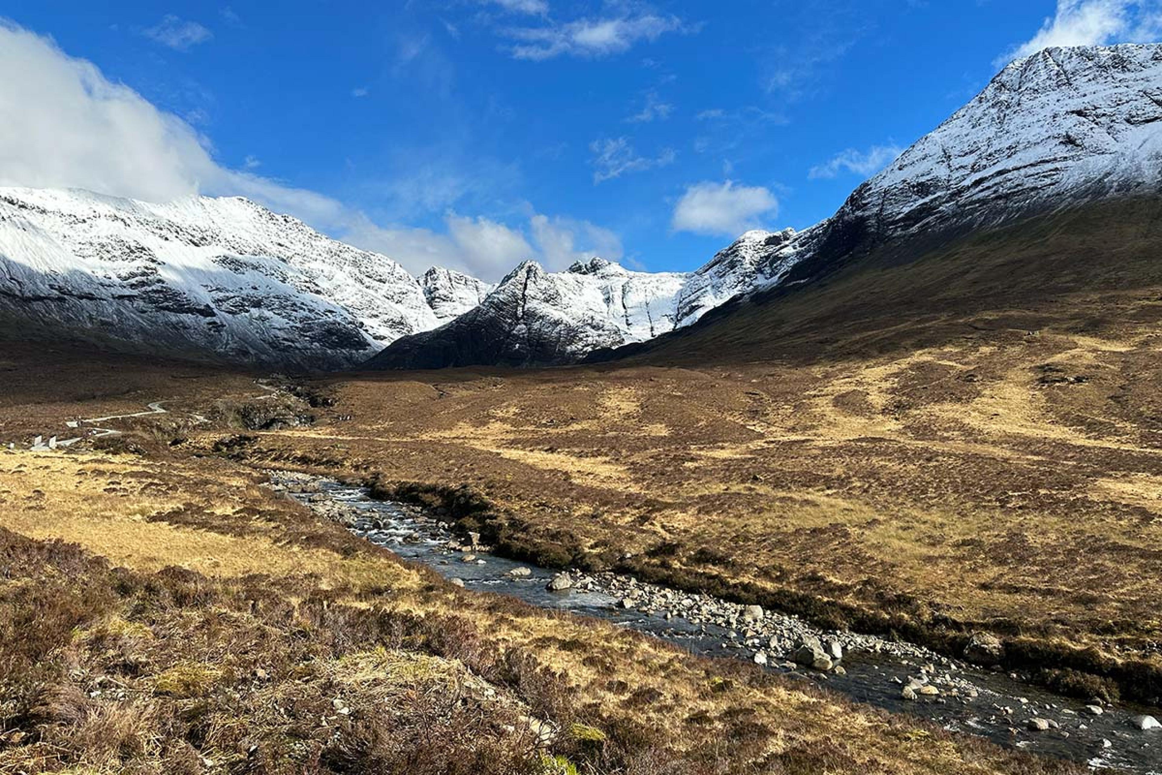 stream cutting through the golden landscape with snowy mountains in the background