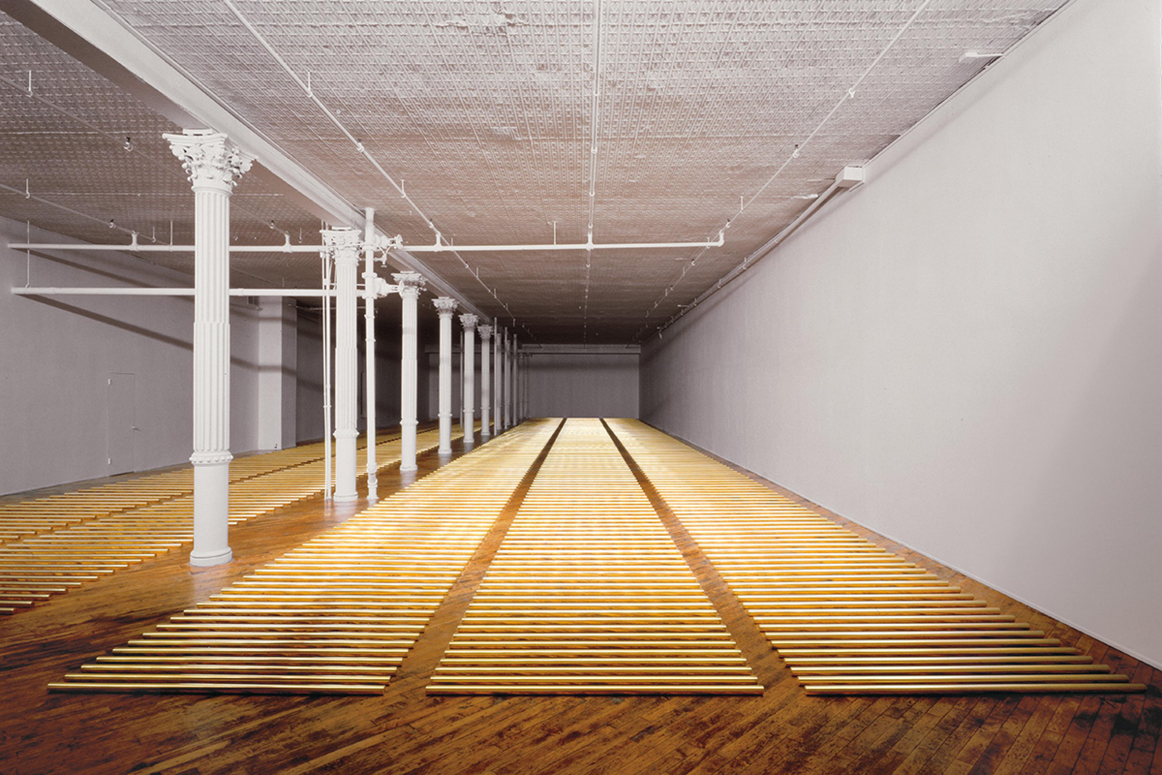an art installation showing hundreds of short brass rods on the floor in neat rows inside an empty space