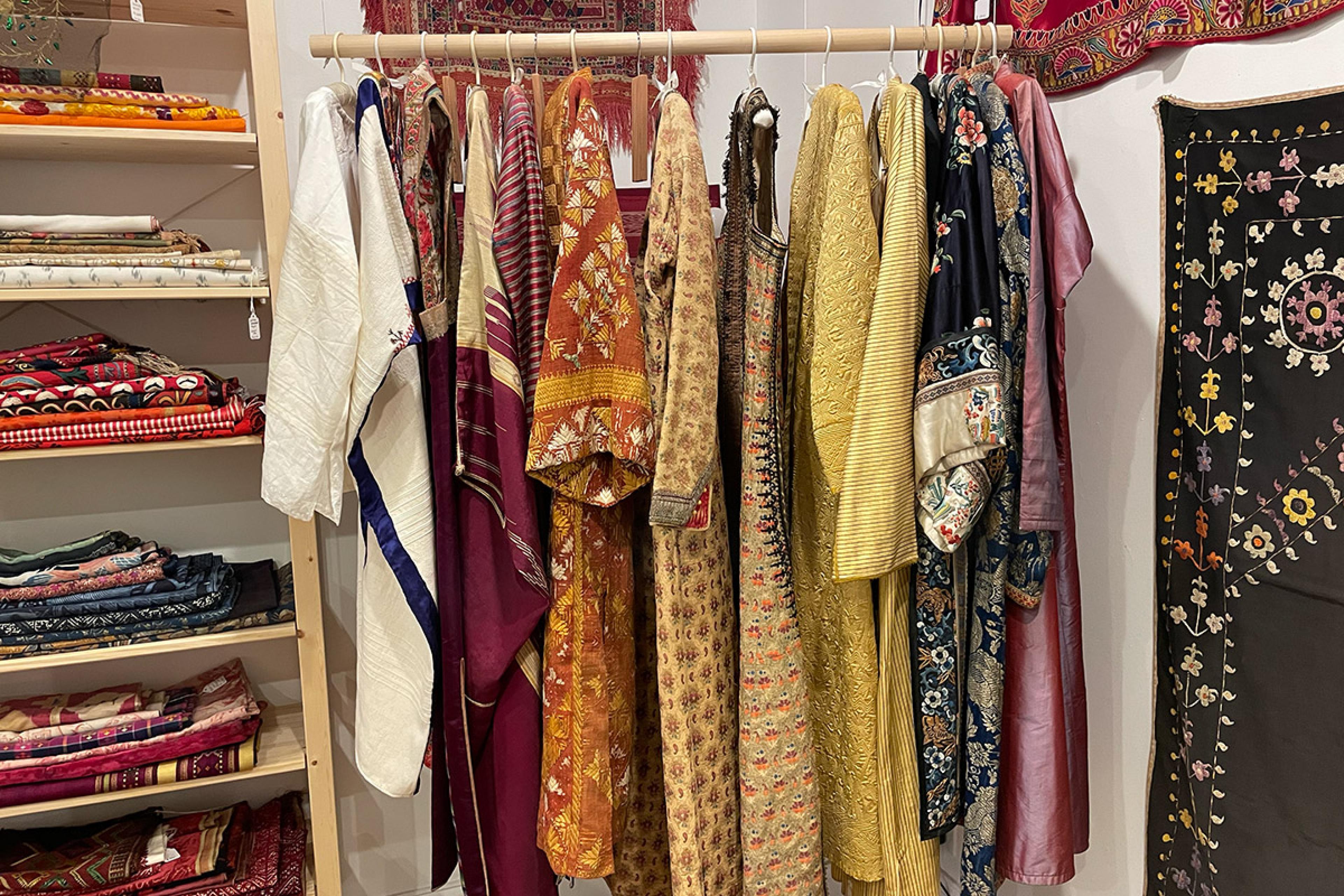 colorful textiles and women's clothing hanging on rack in store