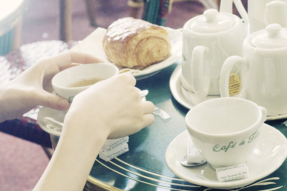 Woman's hands holding tea cup at cafe table with croissant and teapot