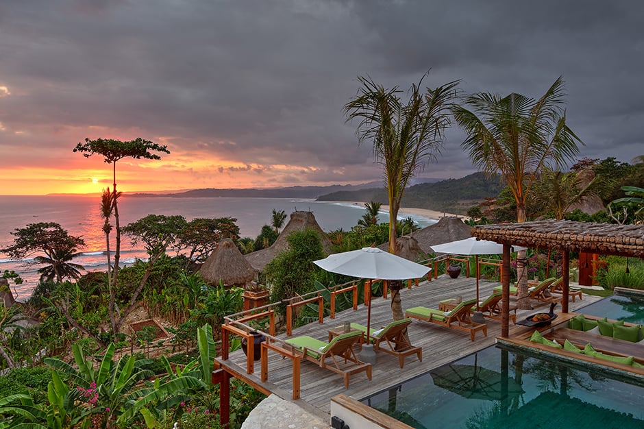 Pool and balcony with lounge chairs overlooking palm trees and beach at sunset at Nihiwatu in Indonesia