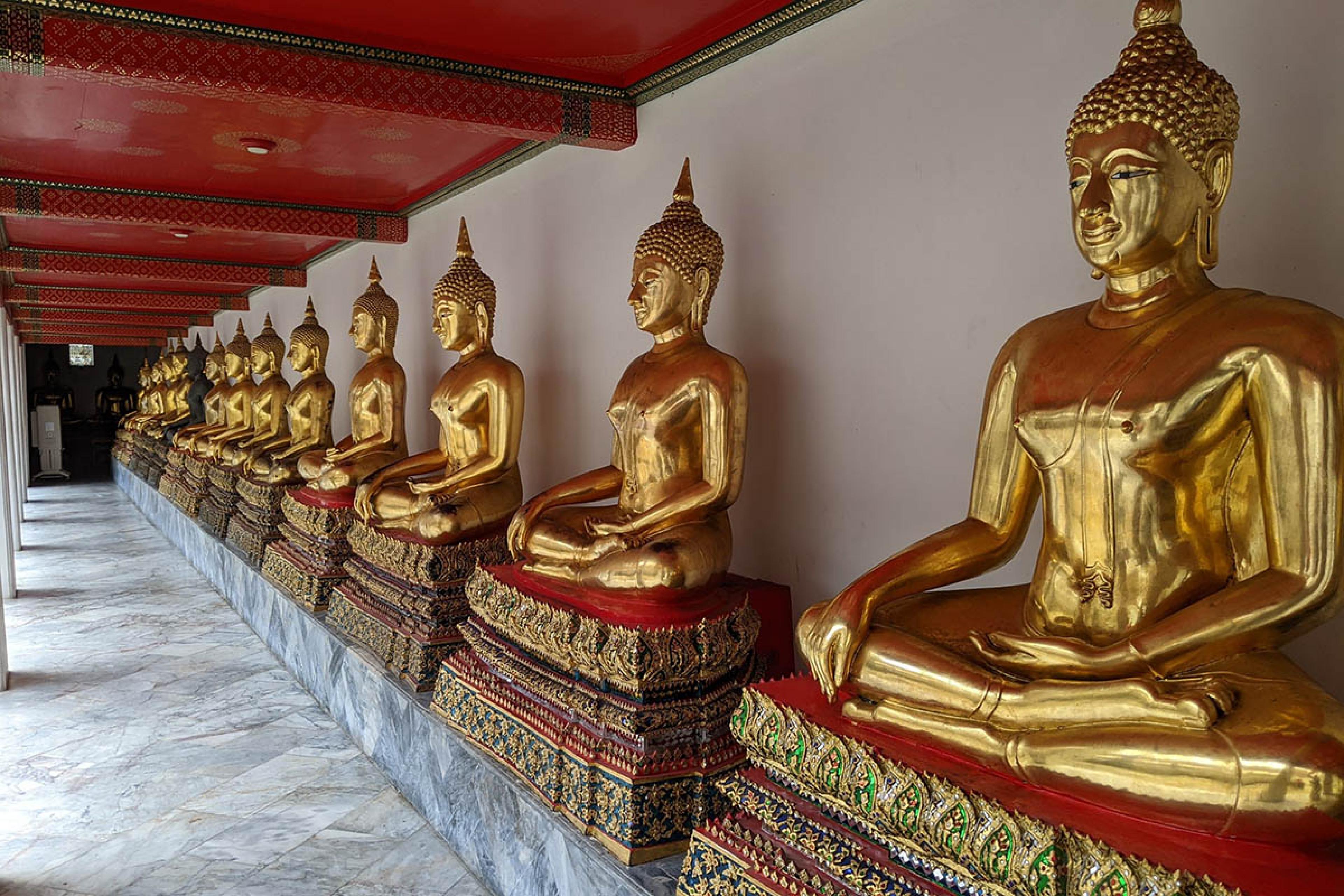gold buddha statues lined up against a temple wall in Bangkok
