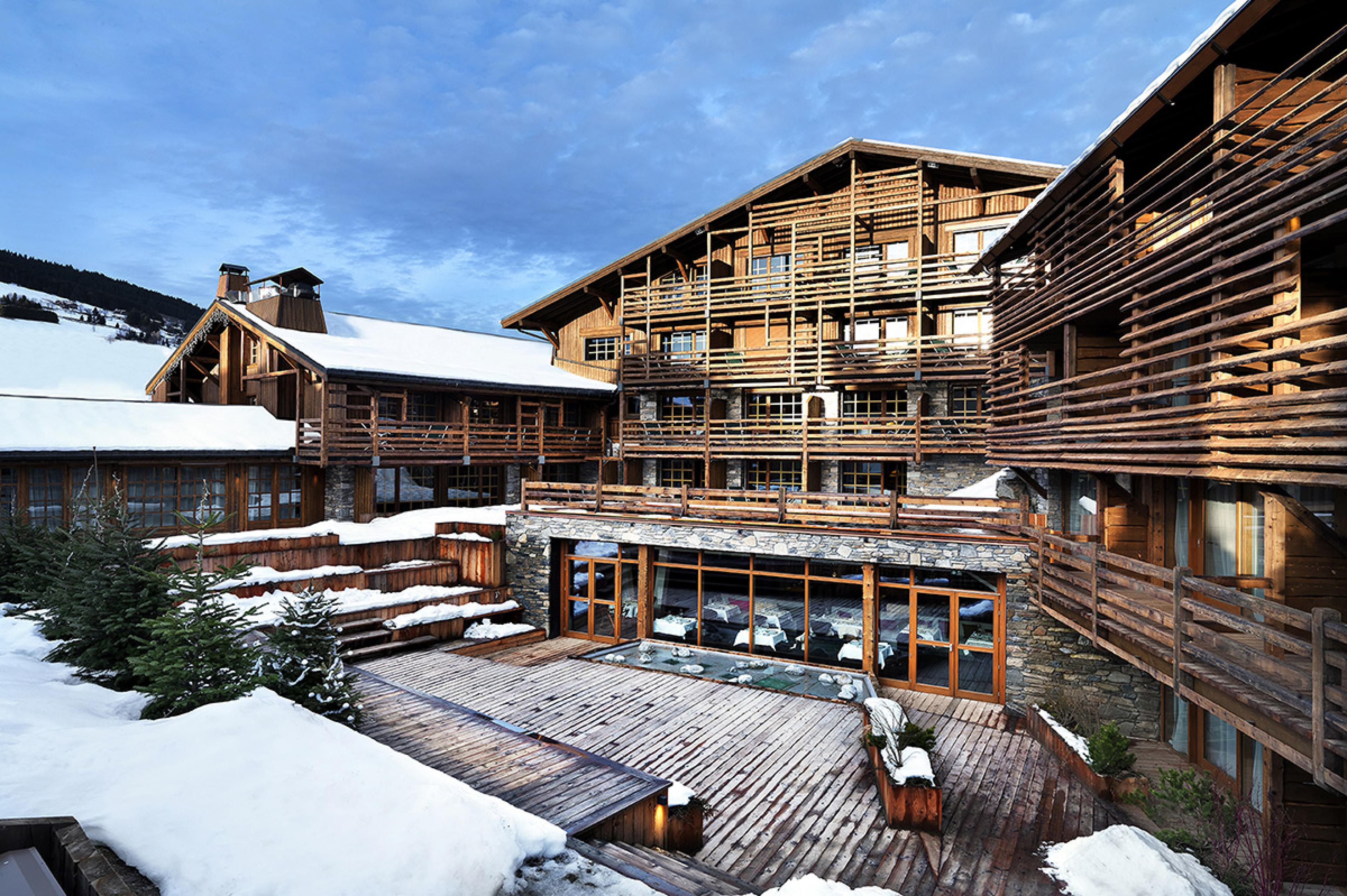 view of chalet hotel with wooden walls and a stone terrace, with a light dusting of snow on ground