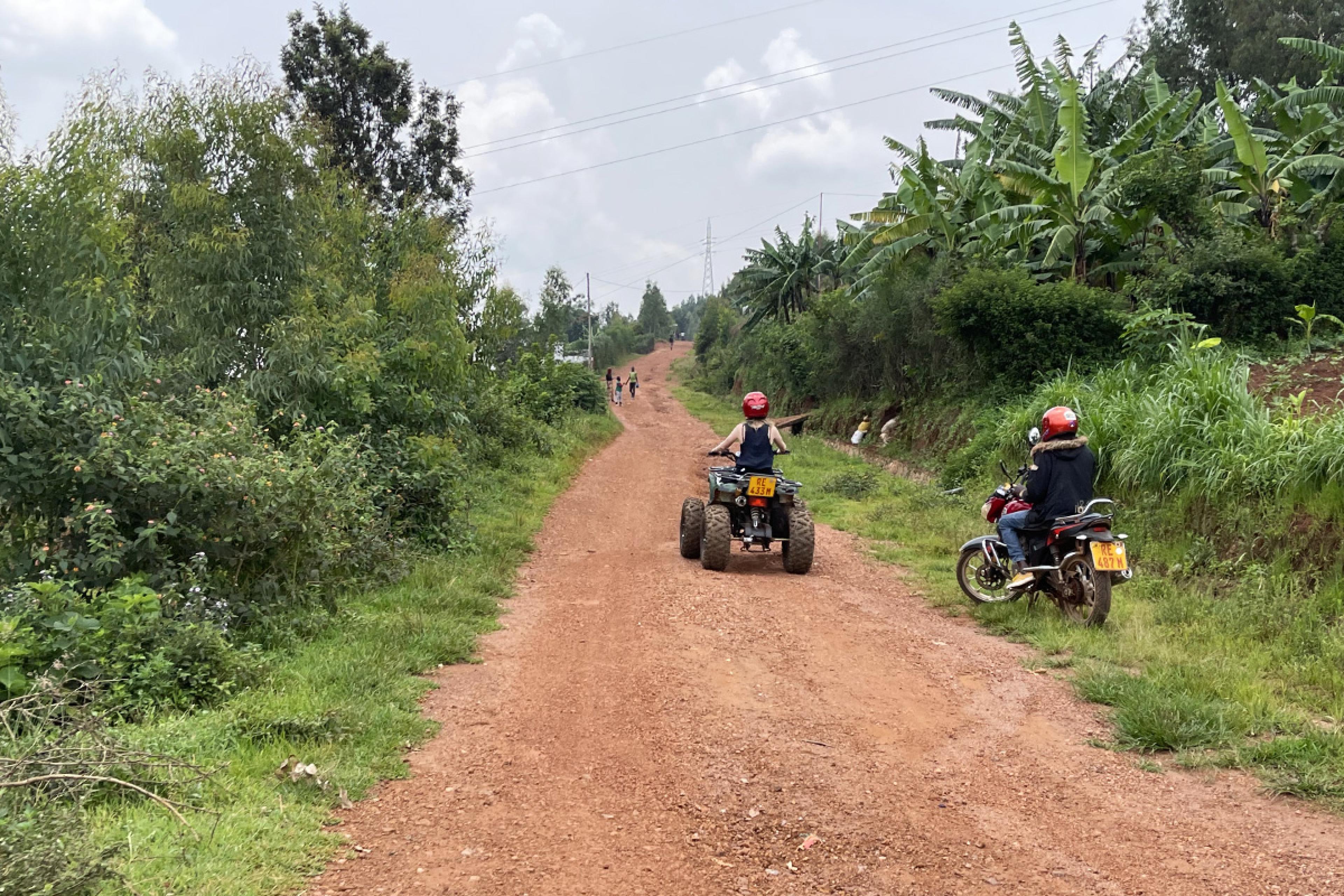 quad biking down a dirt path lined with greenery