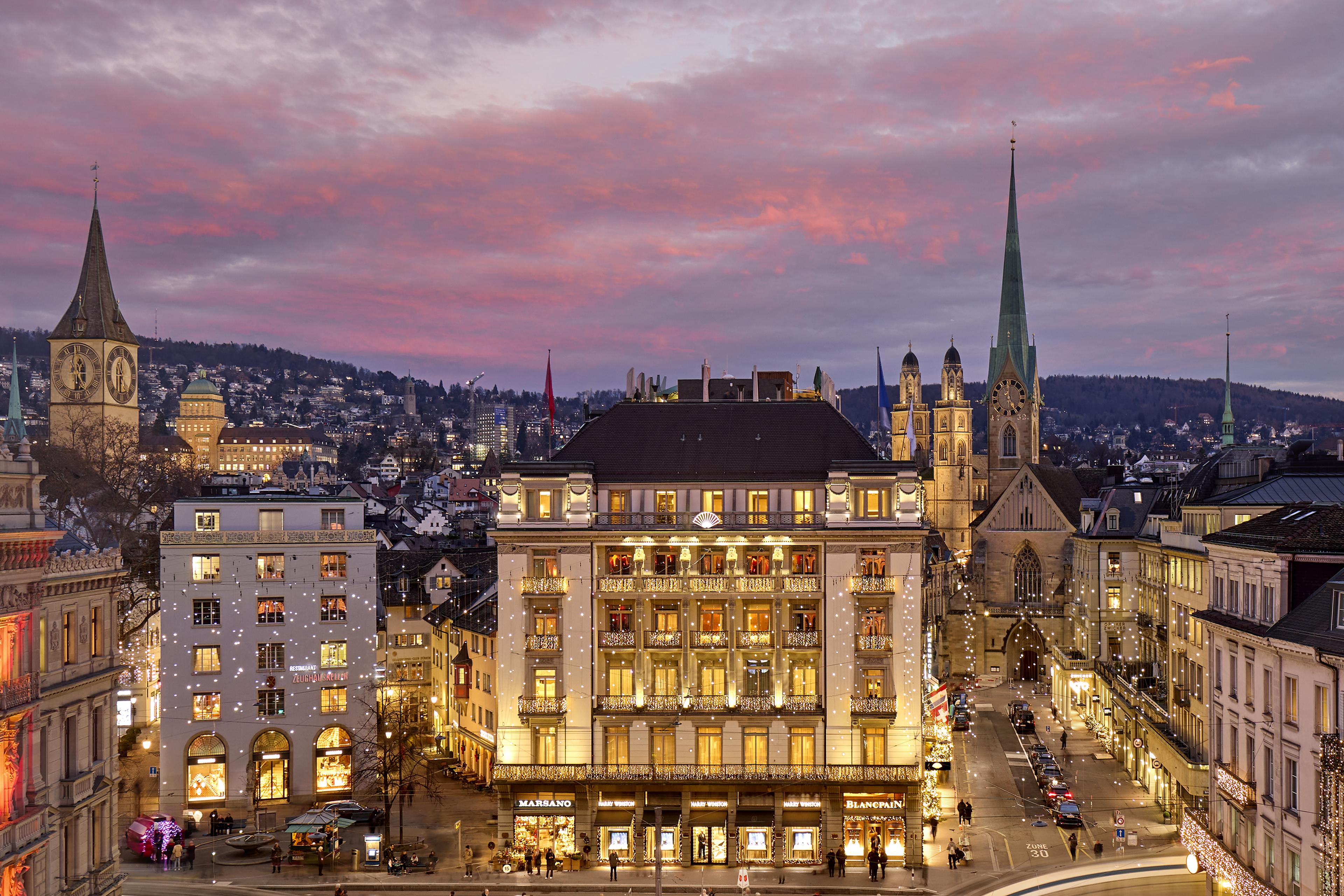 looking at grand hotel building at dusk from across a plaza, with european city Zurich in the background