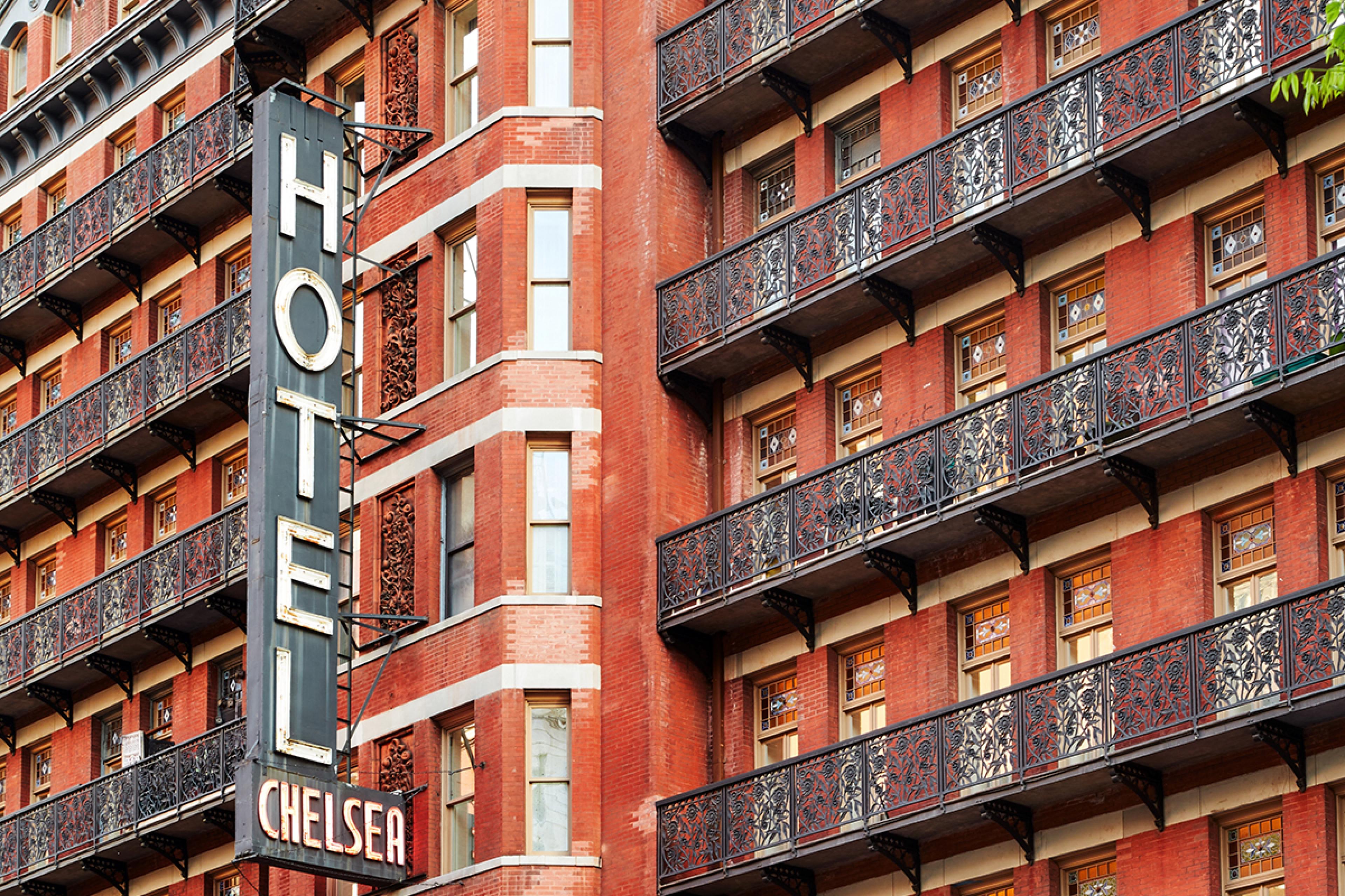exterior of a large brick building with wrought iron fire escape balconies in nyc and a neon sign saying hotel chelsea