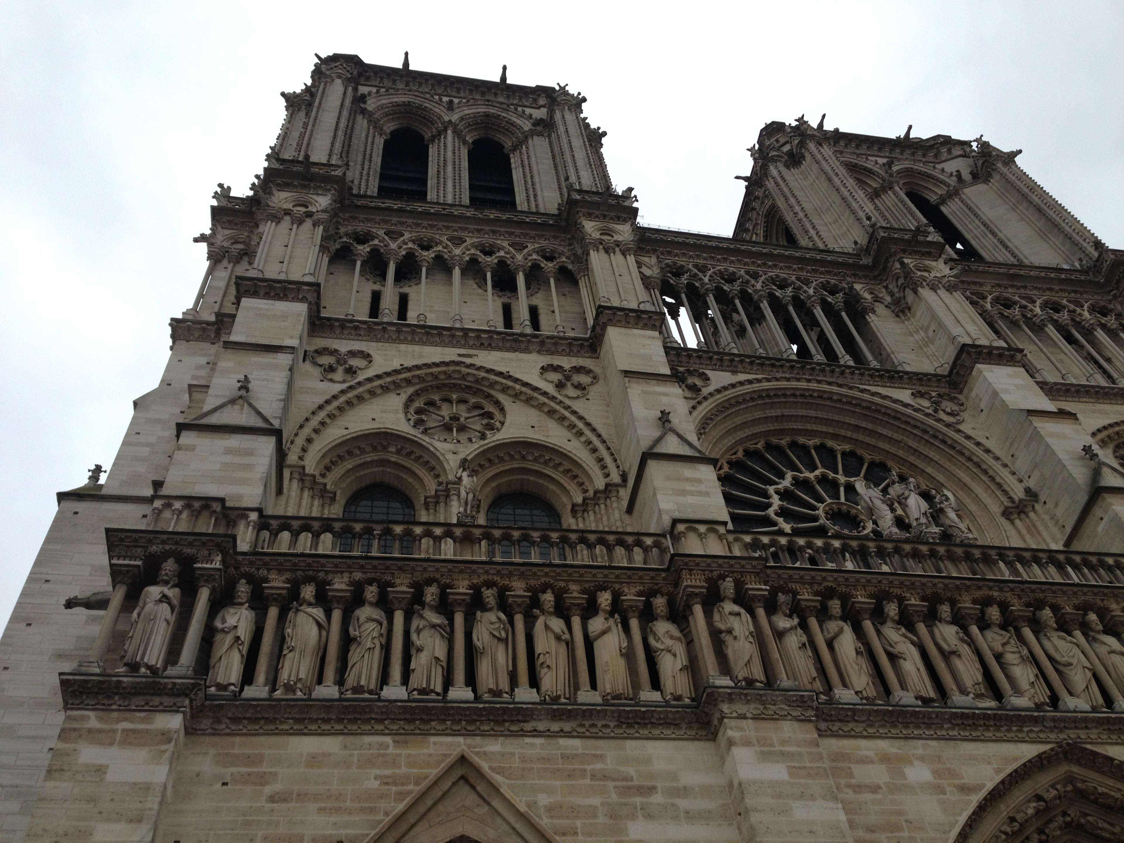 looking up at gothic towers of notre dame on gray sky day in paris