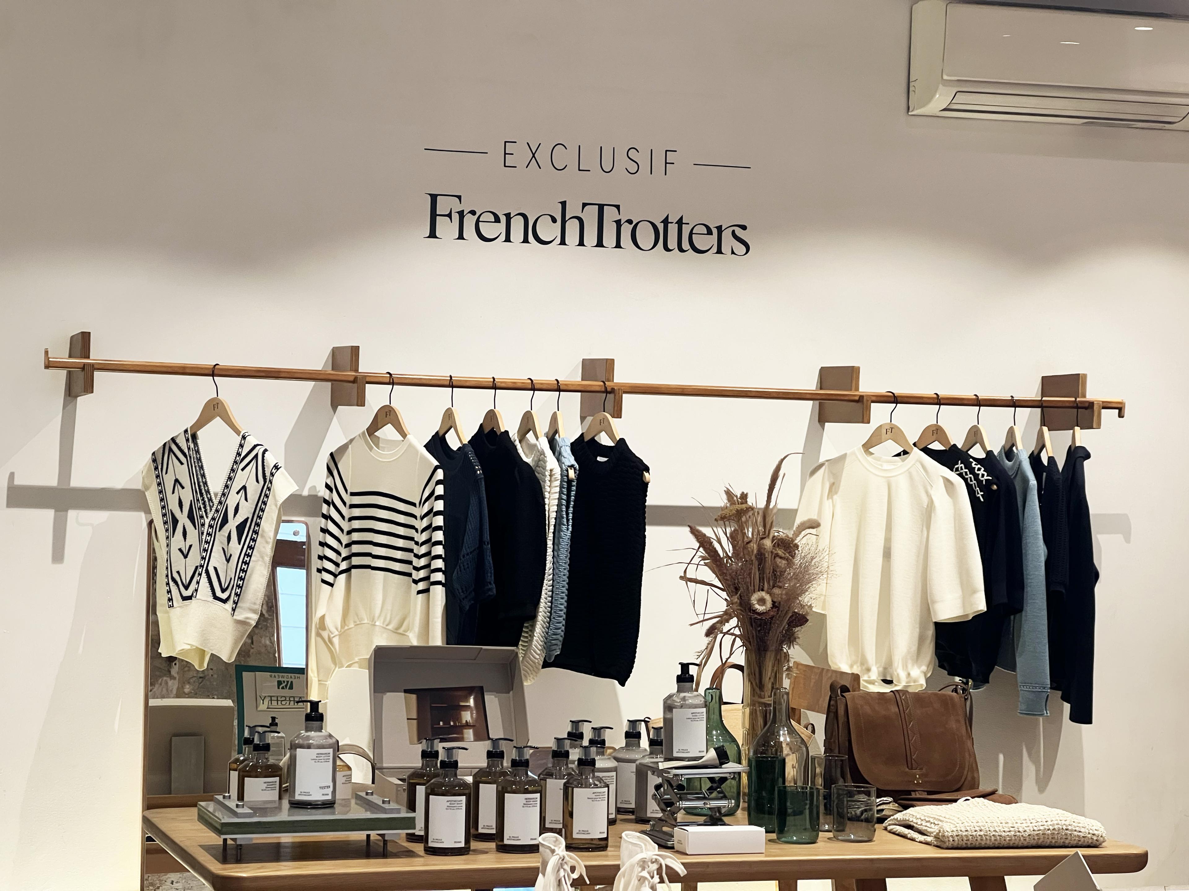 interior of a boutique in paris with clothes on wooden clothing rack against a wall with a sign reading FrenchTrotters