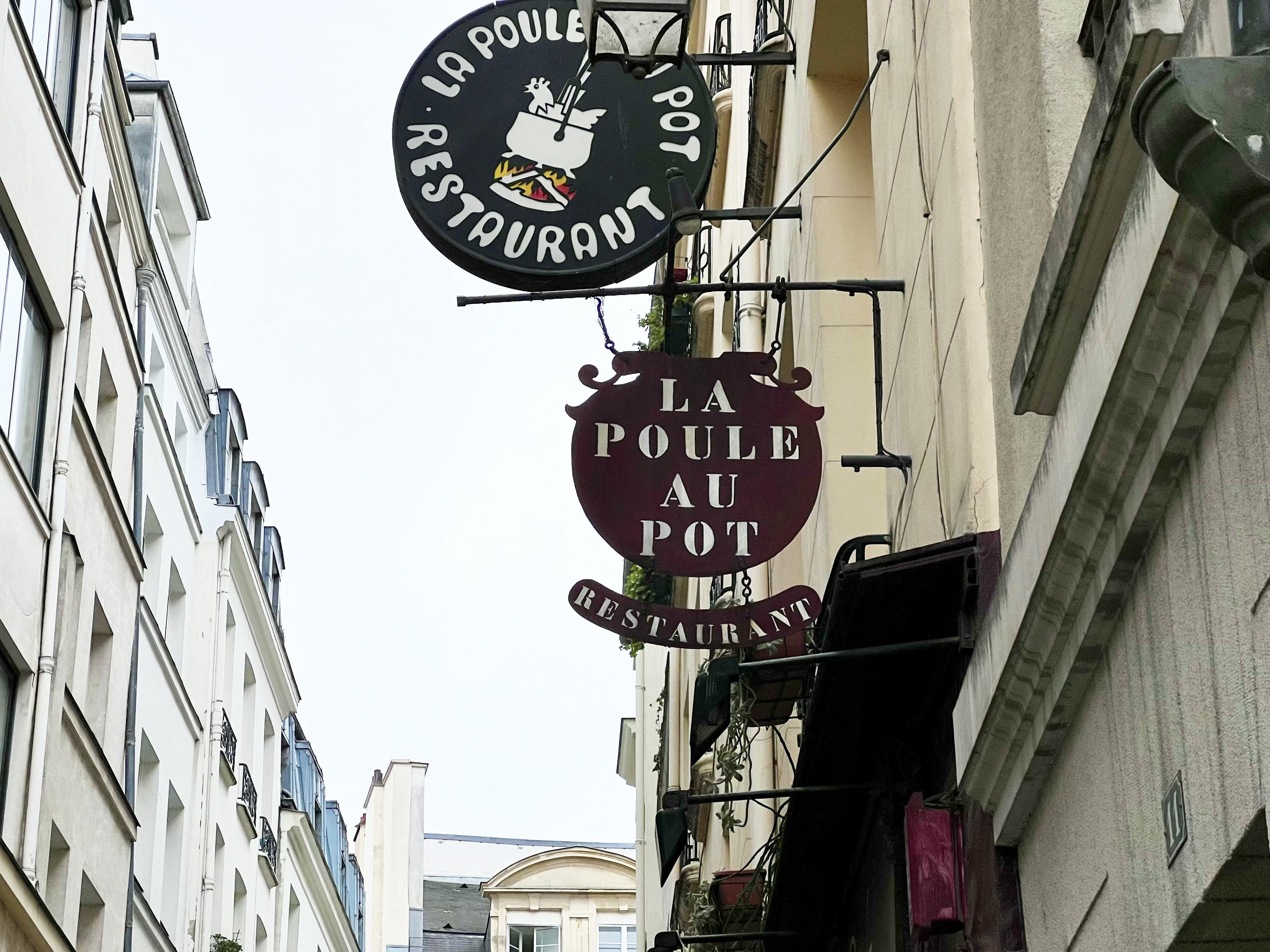 looking up in paris at metal restaurant signs hanging out of building that say La Poule Au Pot  