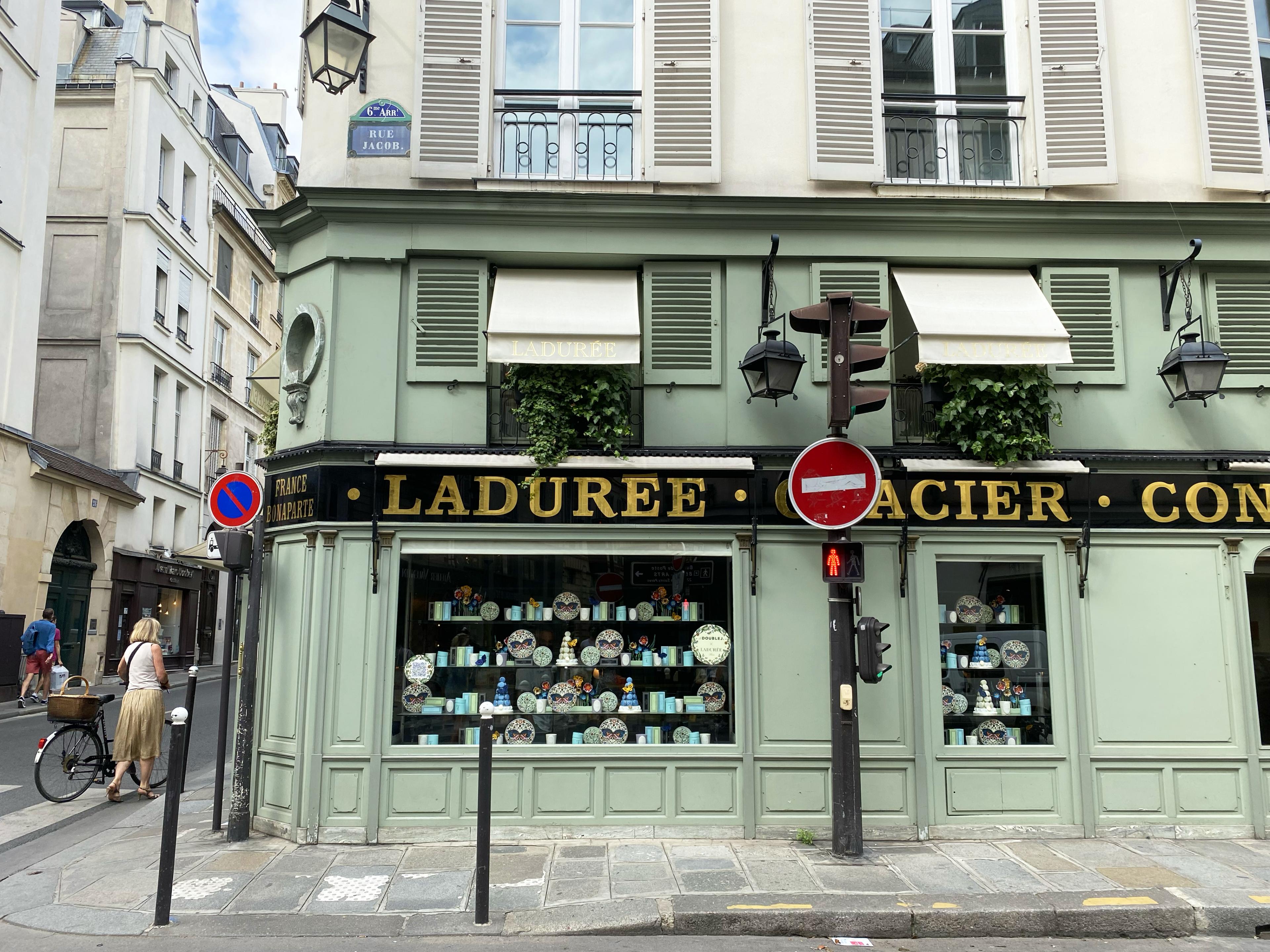 exterior of Laduree shop in Paris on a charming side street with woman walking a bicycle on the left