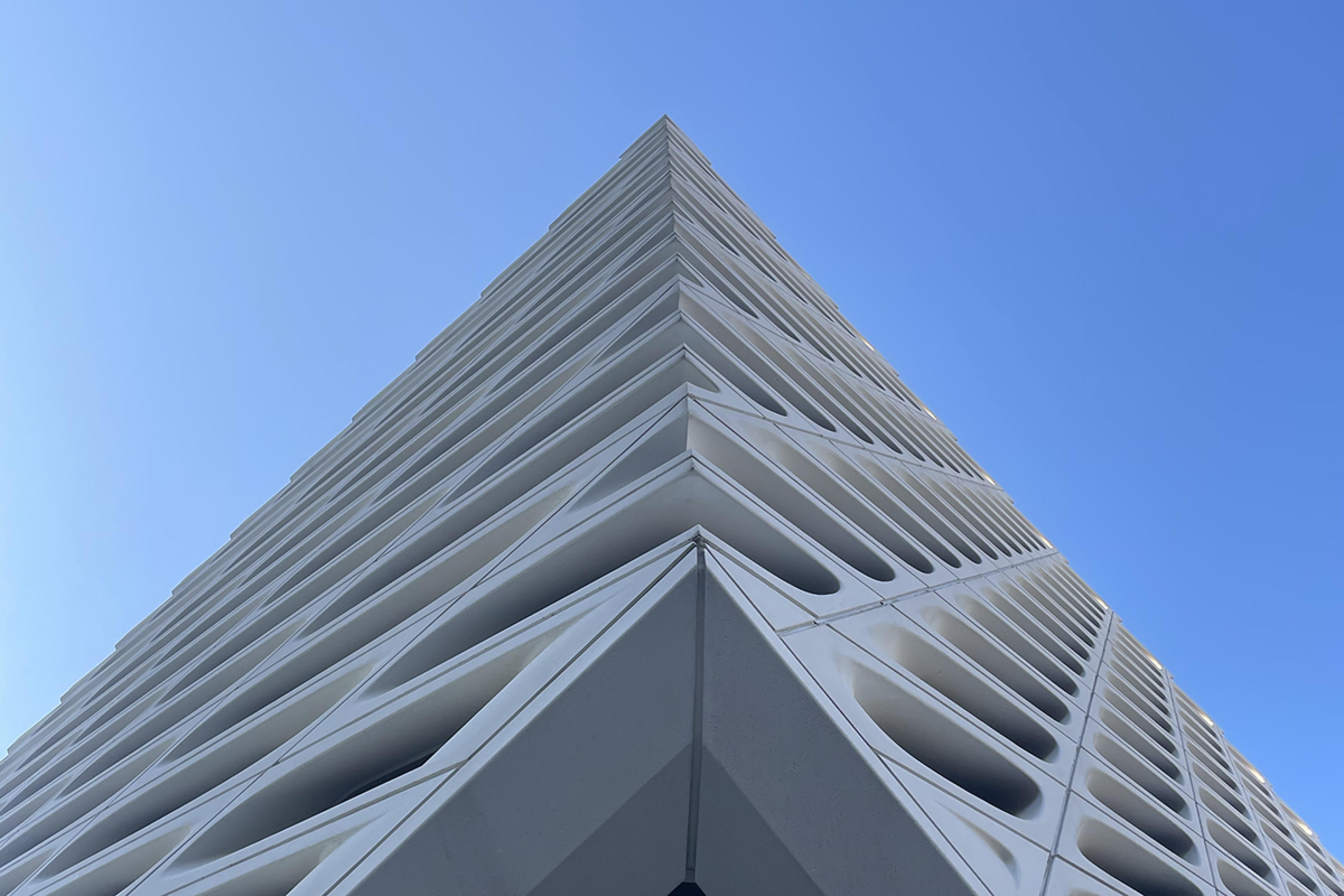 looking up at a the corner of white building with honeycomb-like wholes in it on a blue-sky day