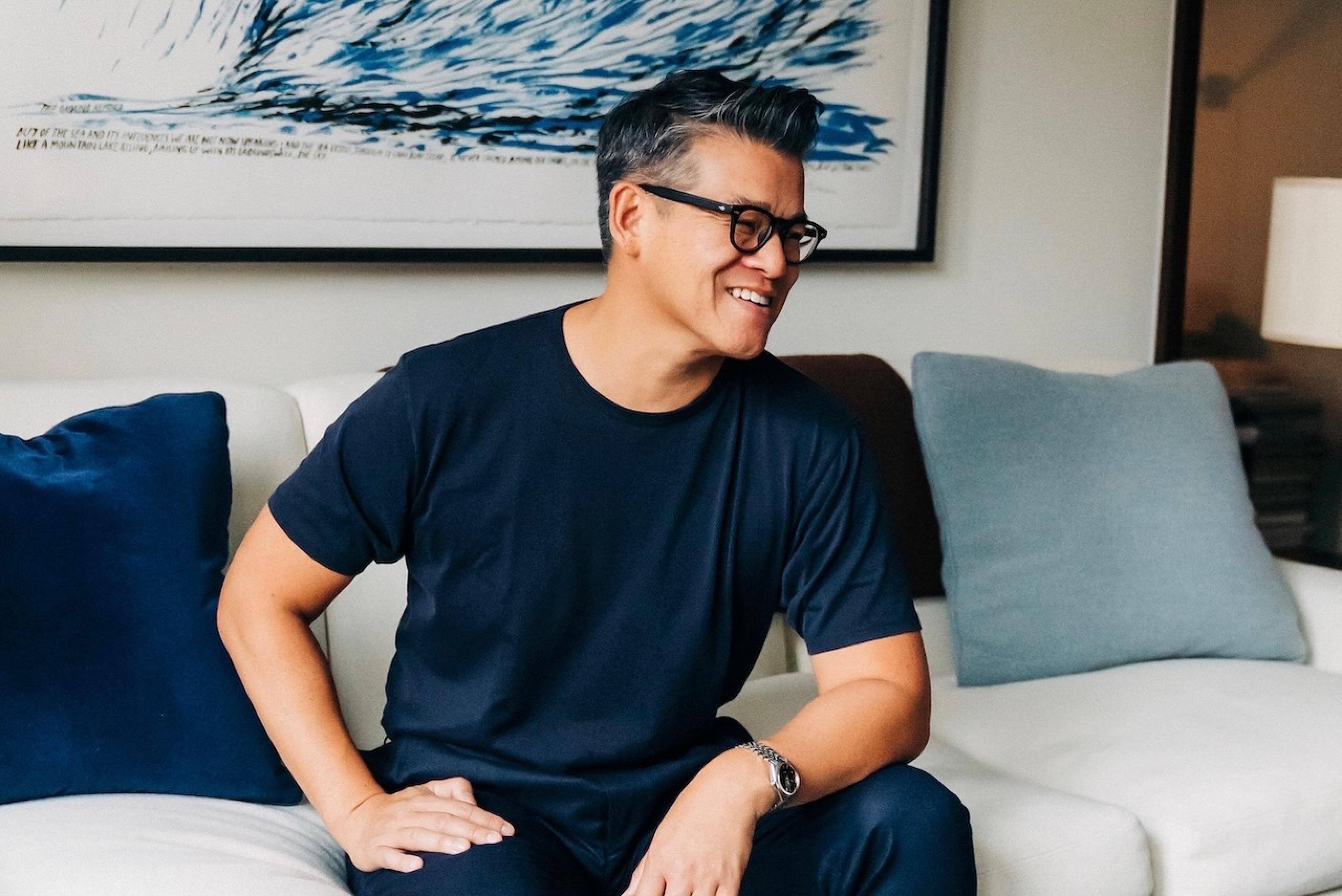 man in glasses sitting by coffee table smiling