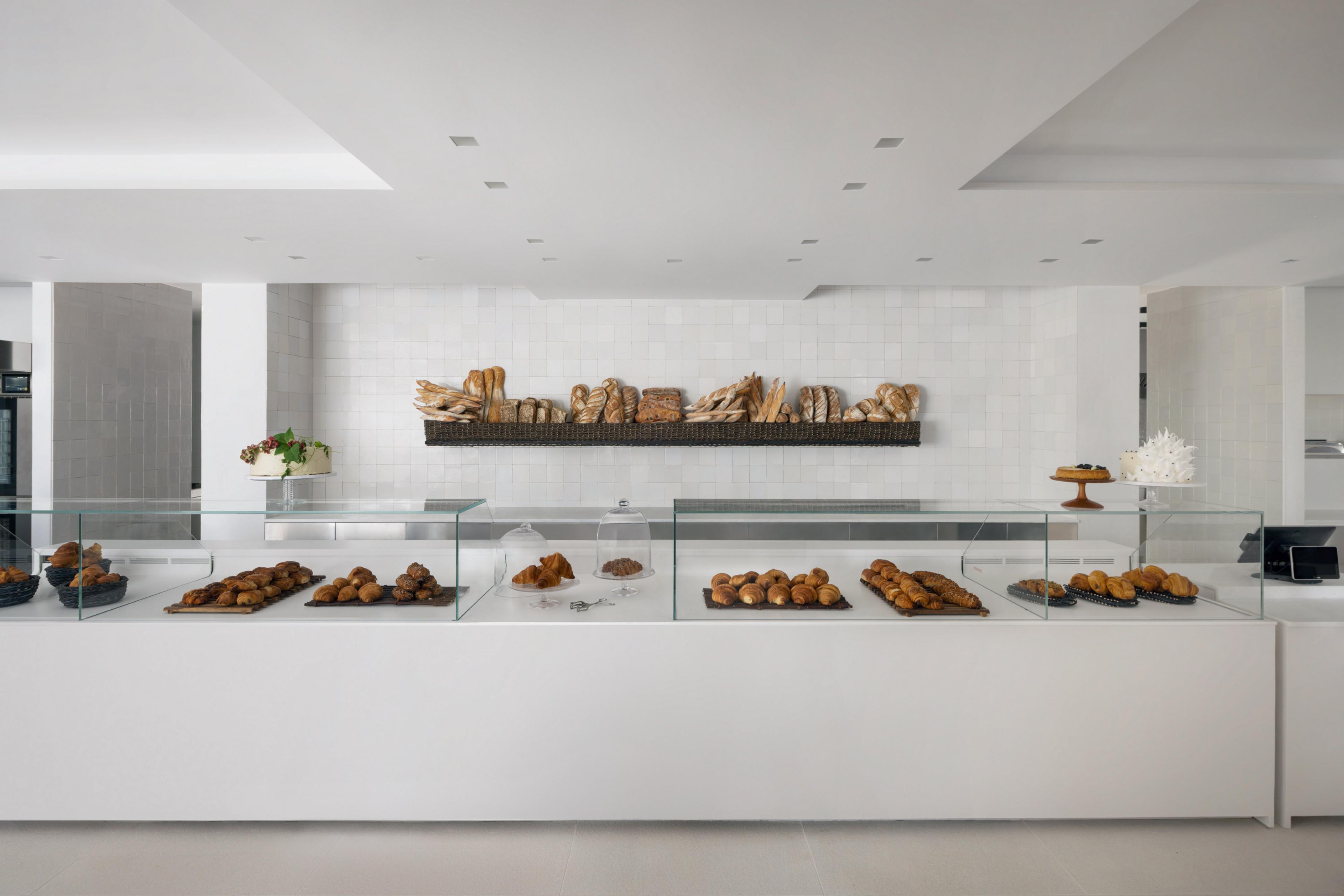 minimalist interior of a white-walled bakery displaying artisinal breads against wall
