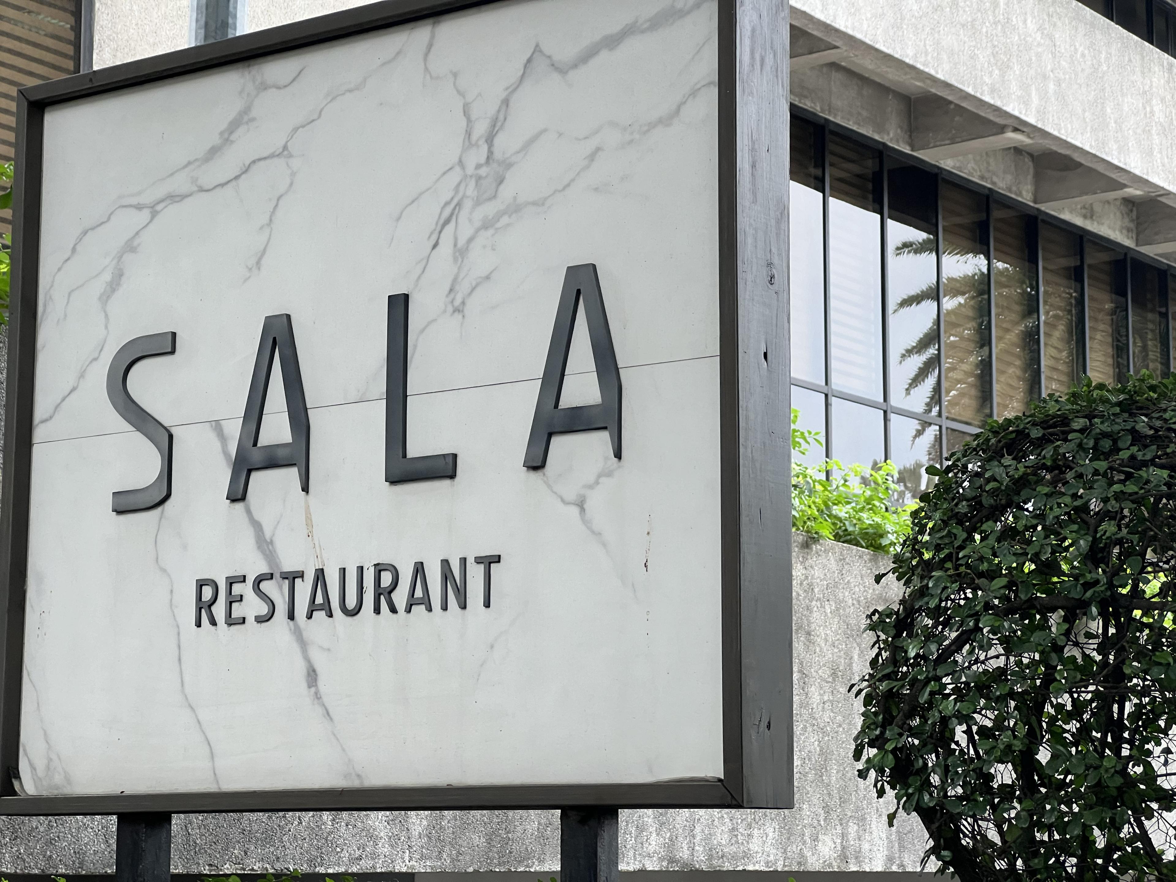 sign in front of white wall noting the entrance to a restaurant called Sala Restaurant