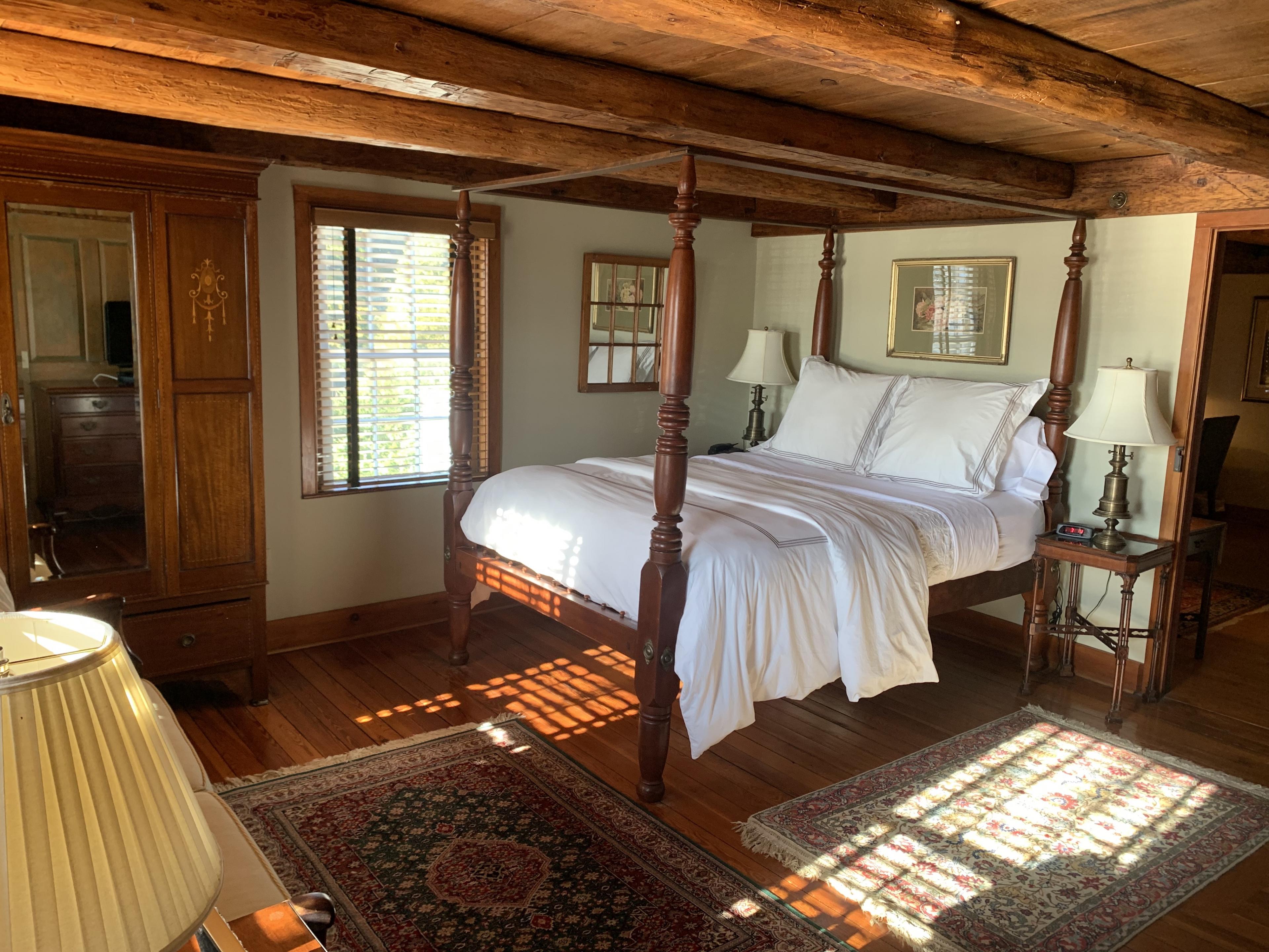 hotel bedroom in traditional old american style with wooden beamed ceiling, four poster wooden bed with white linens
